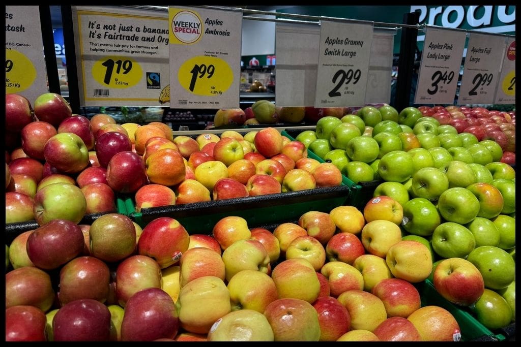 Display of Ambrosia, Granny Smith, Pink Lady, and Fuji apples at a Calgary grocery store with price tags highlighting food costs.