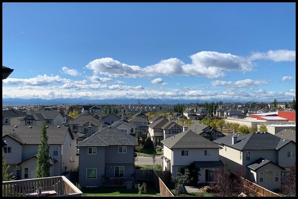 Suburban Calgary neighbourhood with rows of family homes and scenic views of the Rocky Mountains in the distance.