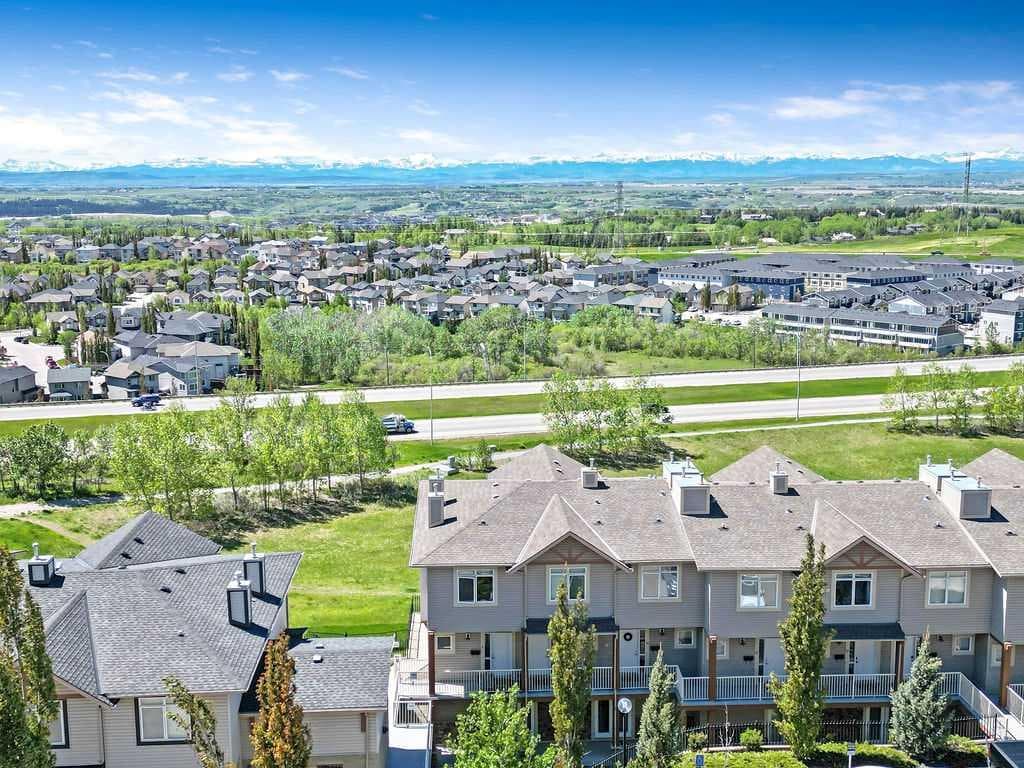Stunning view of Rocky Ridge in Calgary with townhomes in the foreground, rolling green spaces, and the Rocky Mountains in the distance — a perfect blend of suburban living and natural beauty.