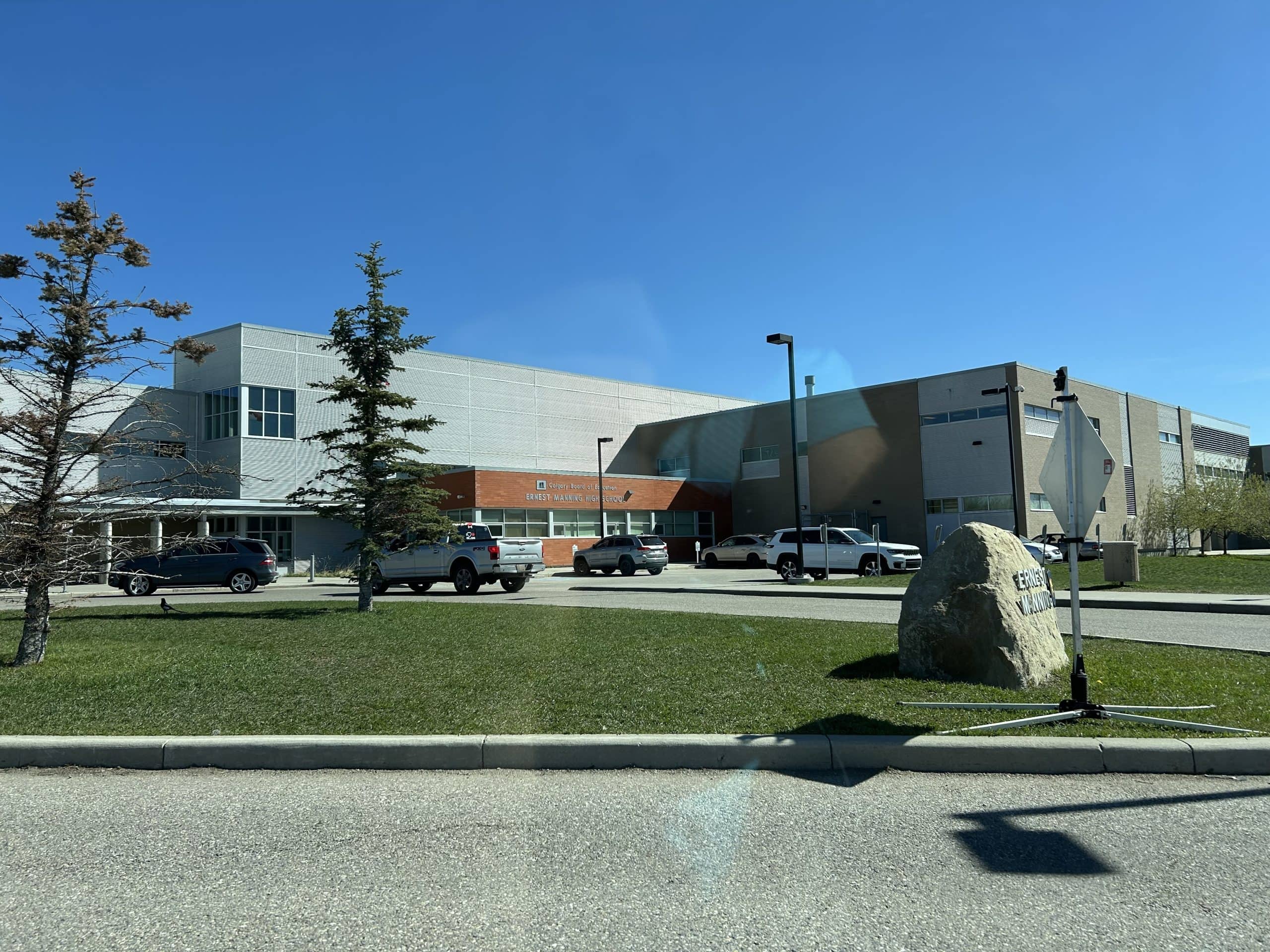 Exterior of Ernest Manning High School in Springbank Hill Calgary, with student parking, modern architecture, and clear blue skies.