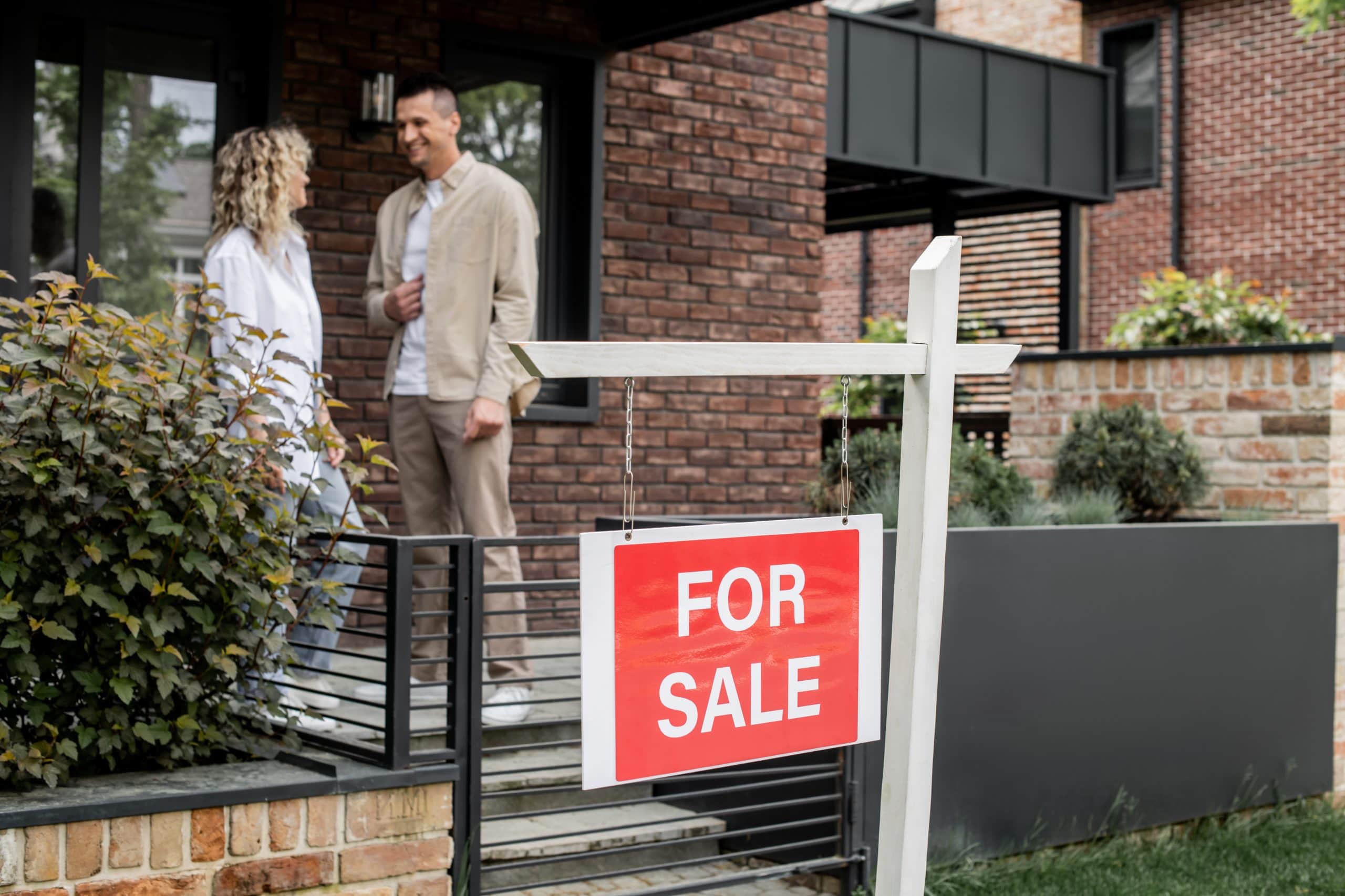 Realtor showing a modern brick home with a 'For Sale' sign out front, highlighting a residential property on the market.