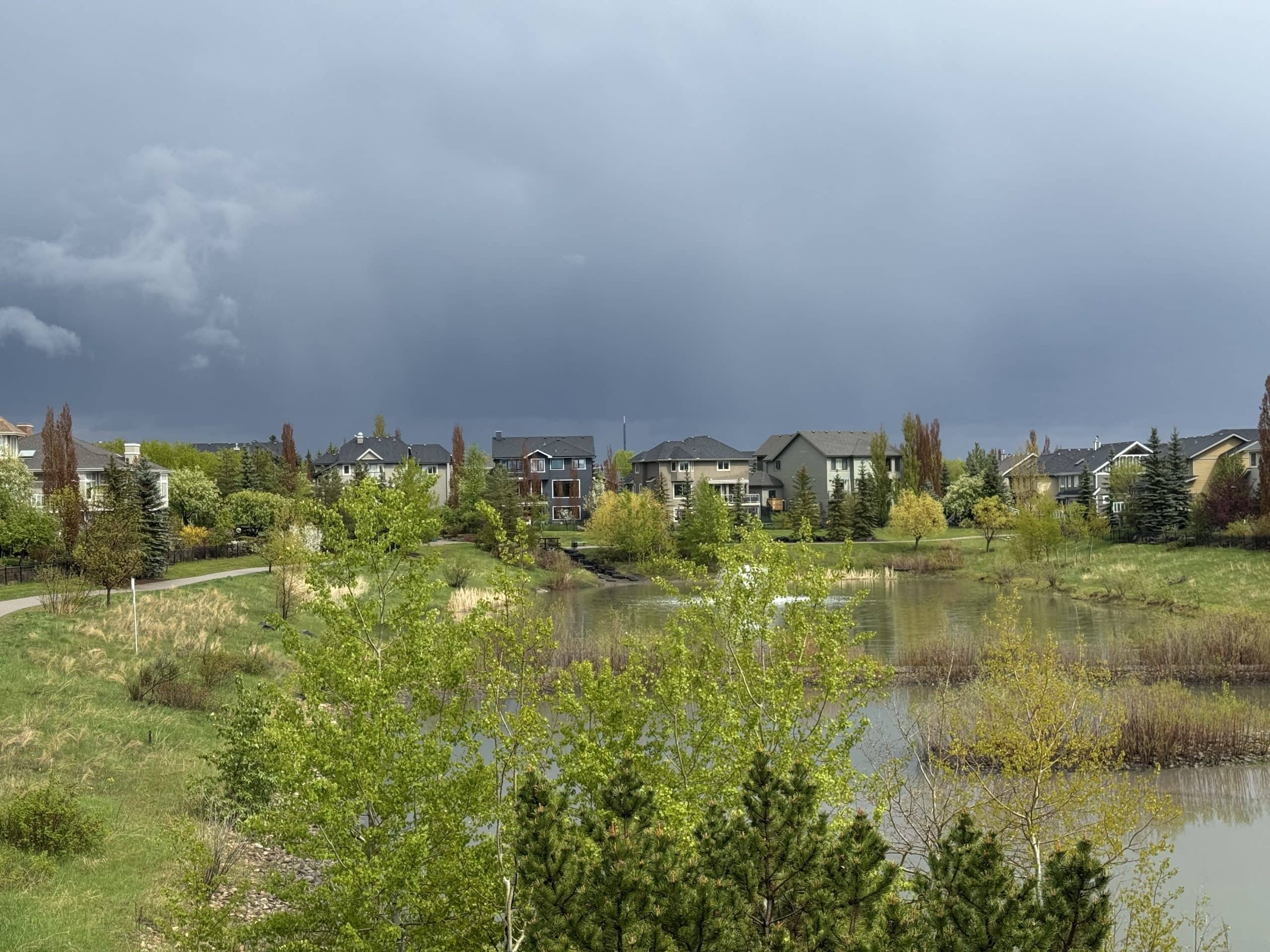 Beautiful pond and walking paths in West Springs Calgary with spacious suburban homes in the background, offering peaceful community living.
