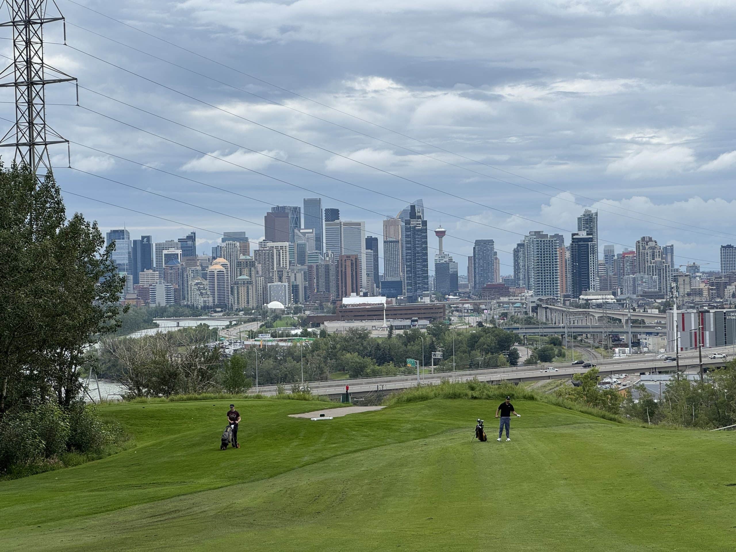 Golfers enjoy a scenic course at Shaganappi Point with a stunning view of the downtown skyline, blending recreation with vibrant city living.