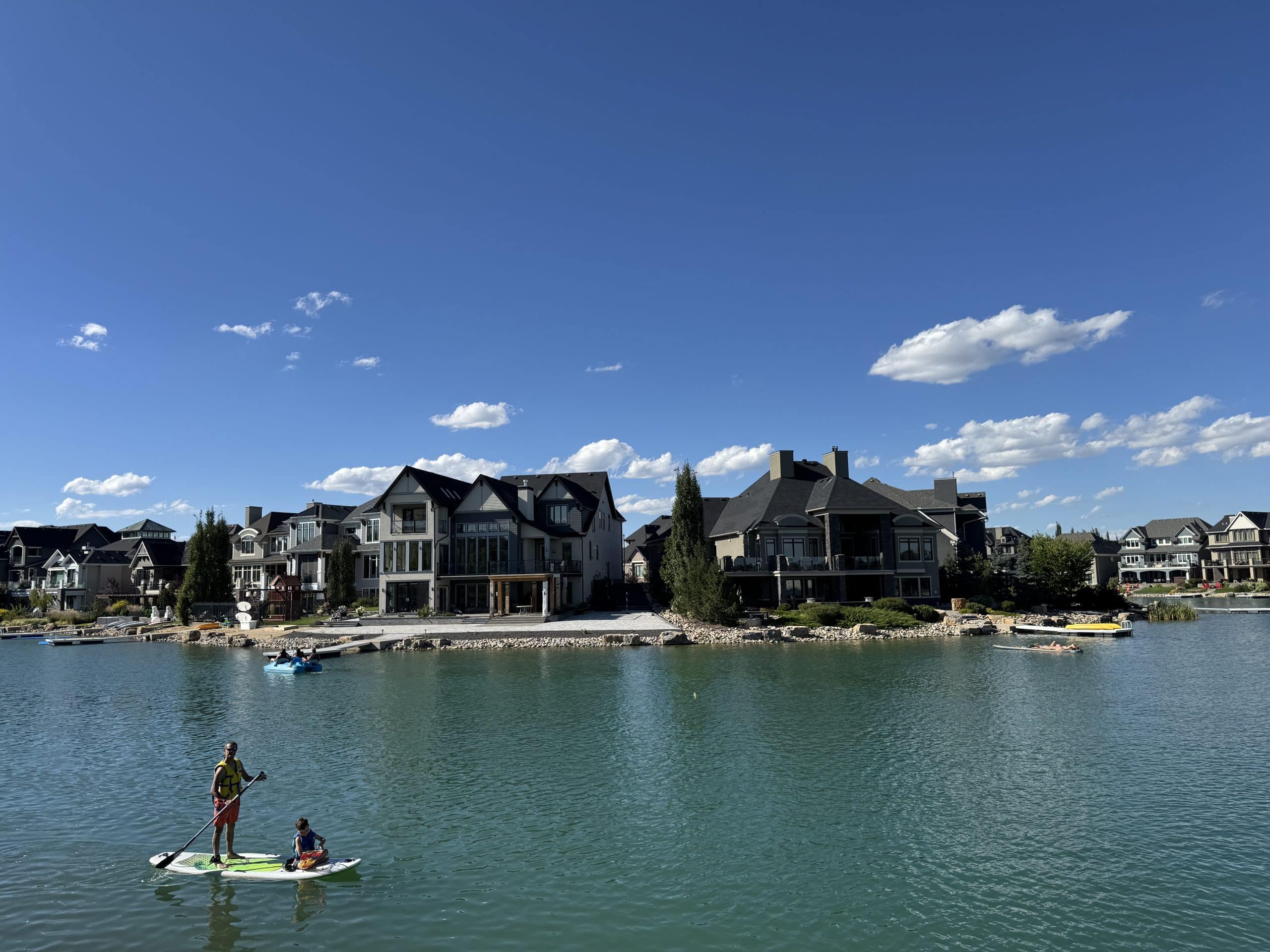 Luxury lakefront homes in Mahogany, Calgary, with residents paddleboarding and enjoying summer on the private community lake.