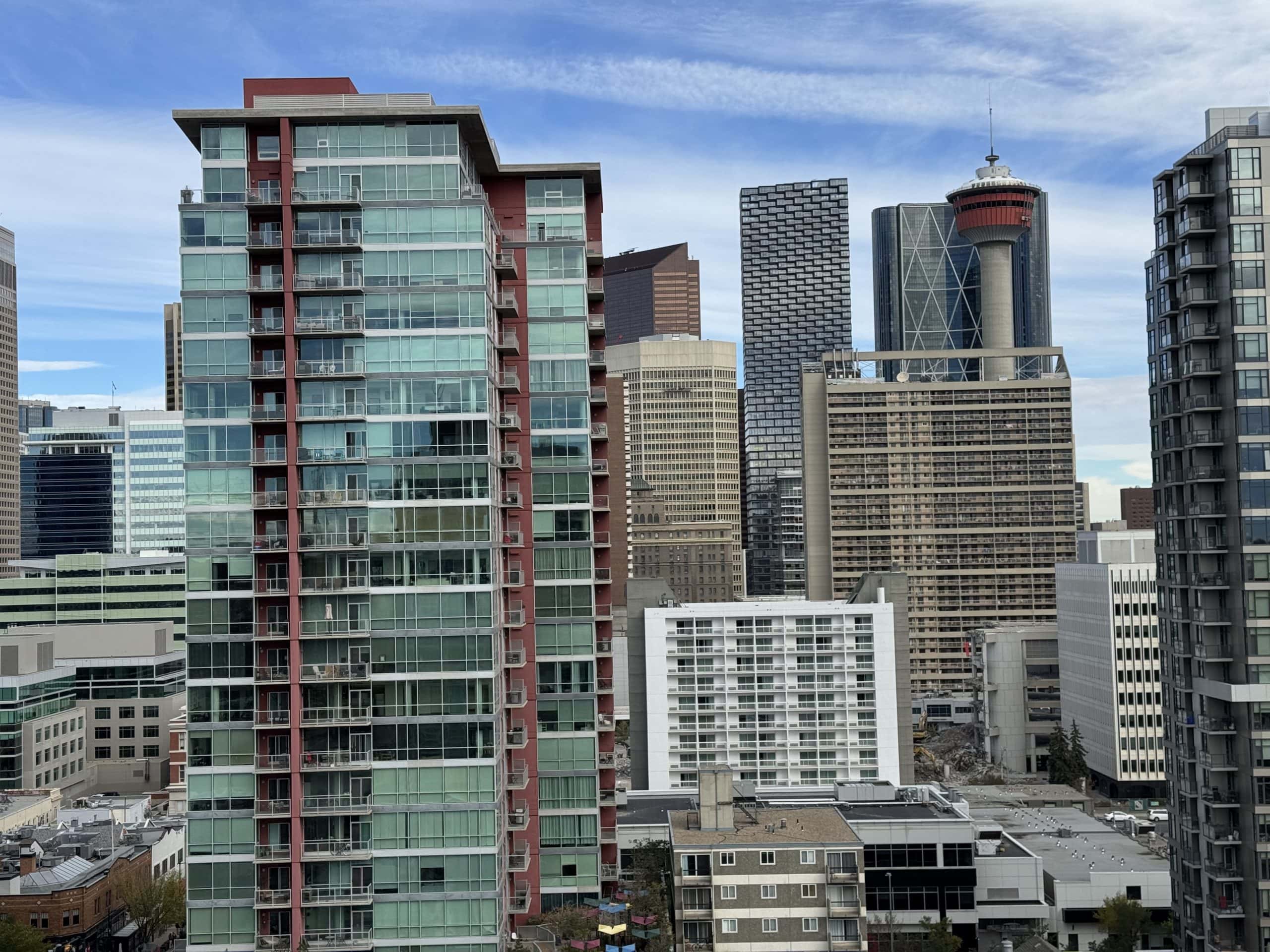 Downtown Calgary skyline with modern high-rise condos, glass towers, and the iconic Calgary Tower under a bright blue sky.