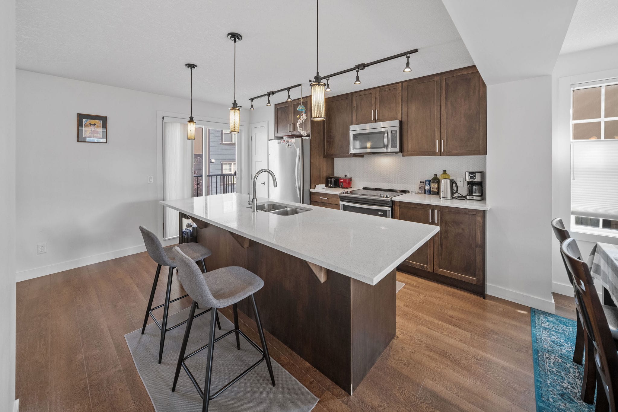 Modern kitchen featuring rich wood cabinetry, sleek quartz countertops, and a large island with seating. Pendant lighting and stainless steel appliances complete the space, creating the perfect blend of style and functionality for cooking and entertaining.