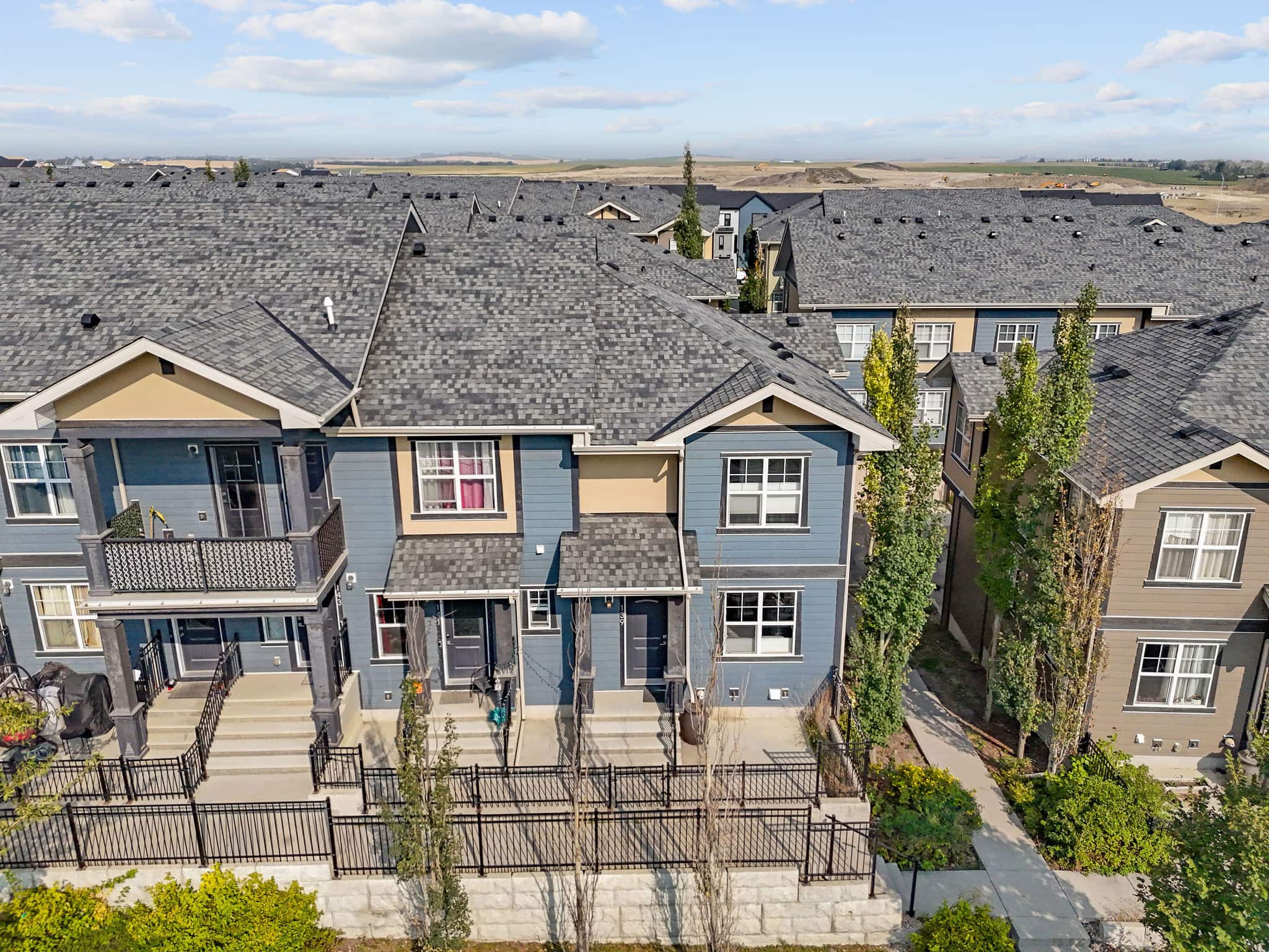 Charming townhome in a well-kept complex in Evanston, Calgary featuring modern blue siding, private fenced front patio, and a welcoming entry. Surrounded by green space and pathways, this home offers a comfortable layout in a desirable community with scenic views nearby.