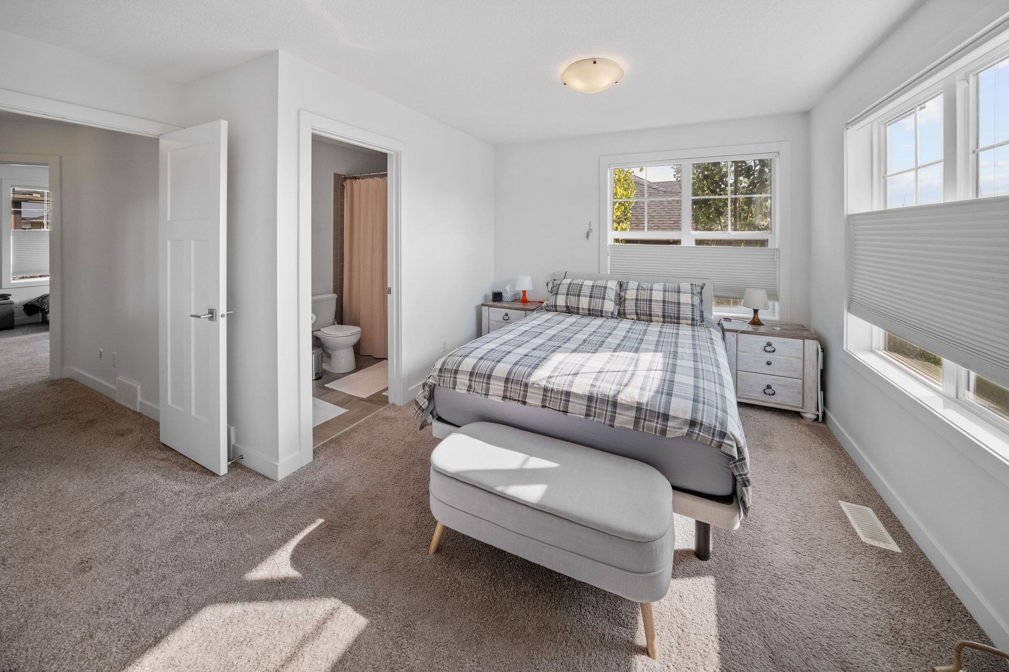 Spacious primary bedroom filled with natural light, featuring large windows, cozy carpeting, and a private ensuite. A comfortable retreat designed for relaxation and convenience.