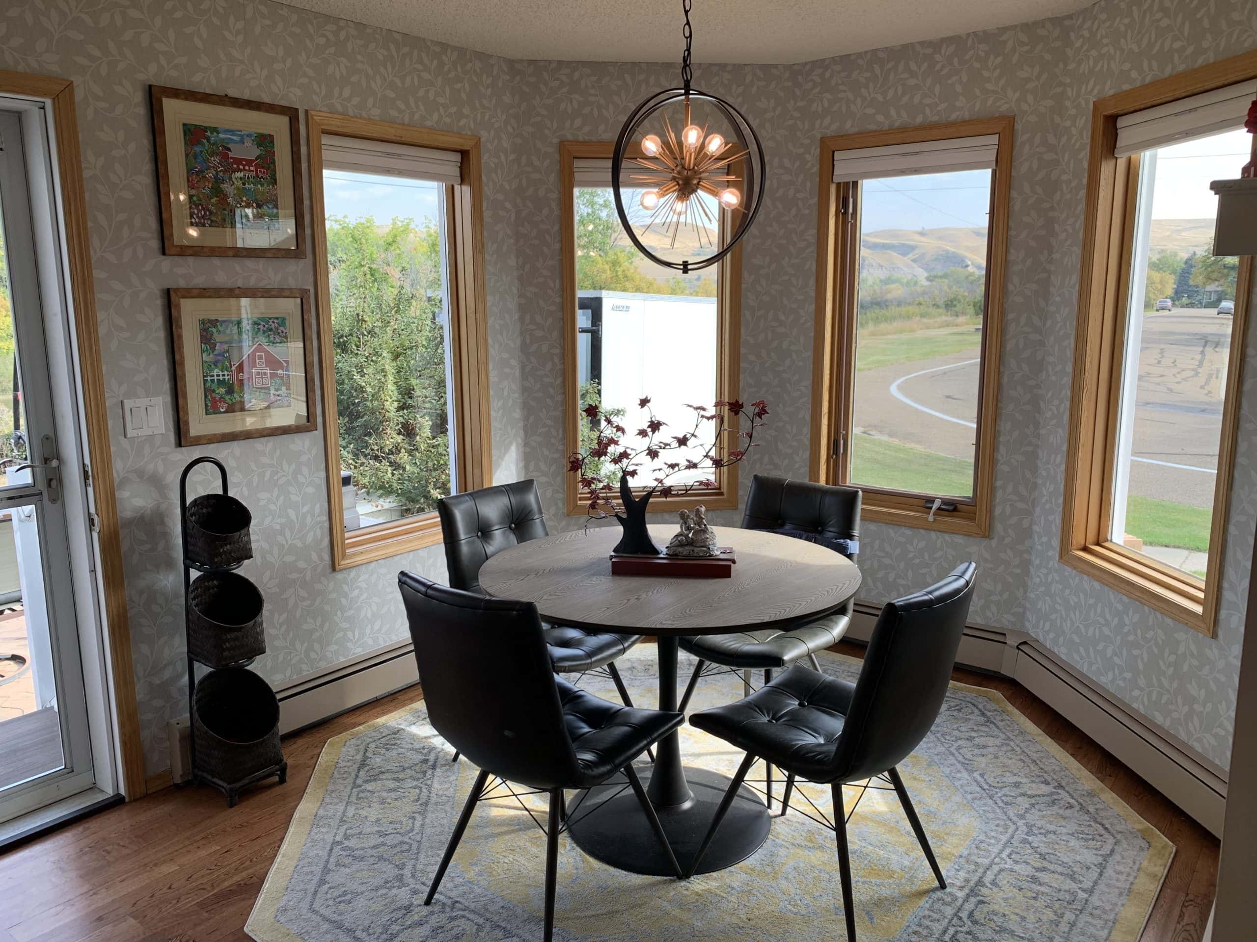 Bright dining nook with wraparound windows, round table, modern chandelier, and scenic views of the surrounding hills and greenery.