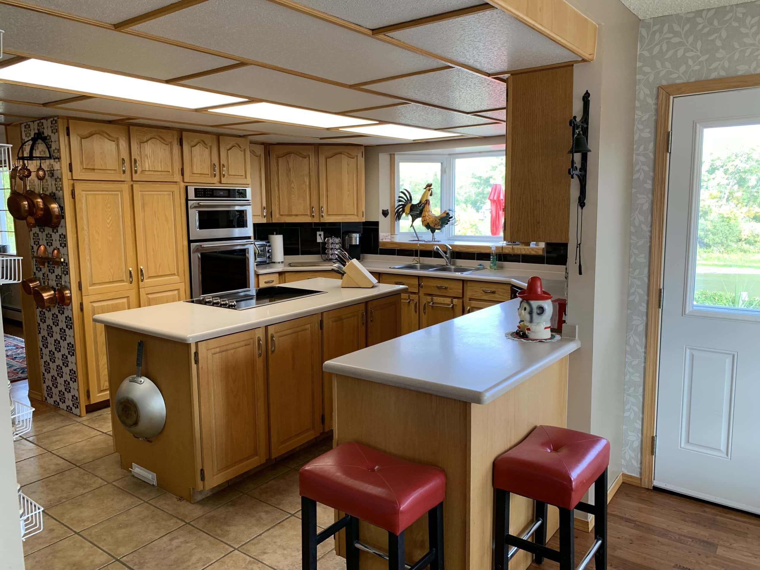 Spacious kitchen with oak cabinets, center island, built-in double ovens, and breakfast bar seating with red stools, accented by large windows bringing in natural light.