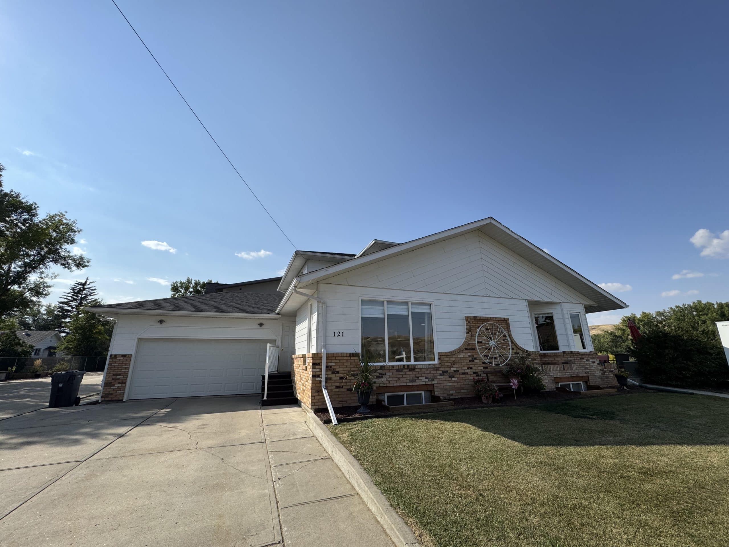 Charming single-family home with brick accents, large front windows, attached double garage, and spacious driveway under a clear blue sky.