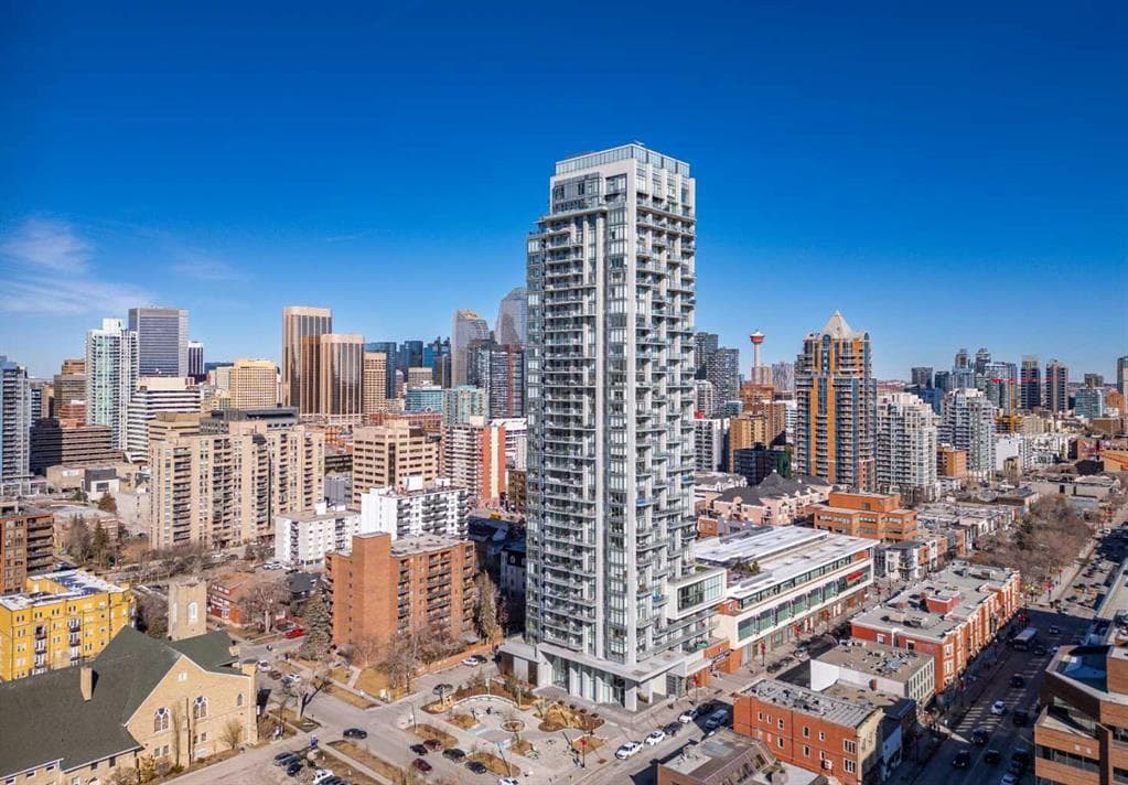 Modern high-rise condominium tower in downtown Calgary, surrounded by the city skyline with the Calgary Tower in the distance on a clear blue sky day.