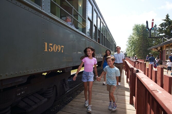 A family walking along the wooden platform beside a vintage train at Heritage Park Historical Village in Calgary, capturing the charm of Canada’s past with its restored railway cars and lively atmosphere.