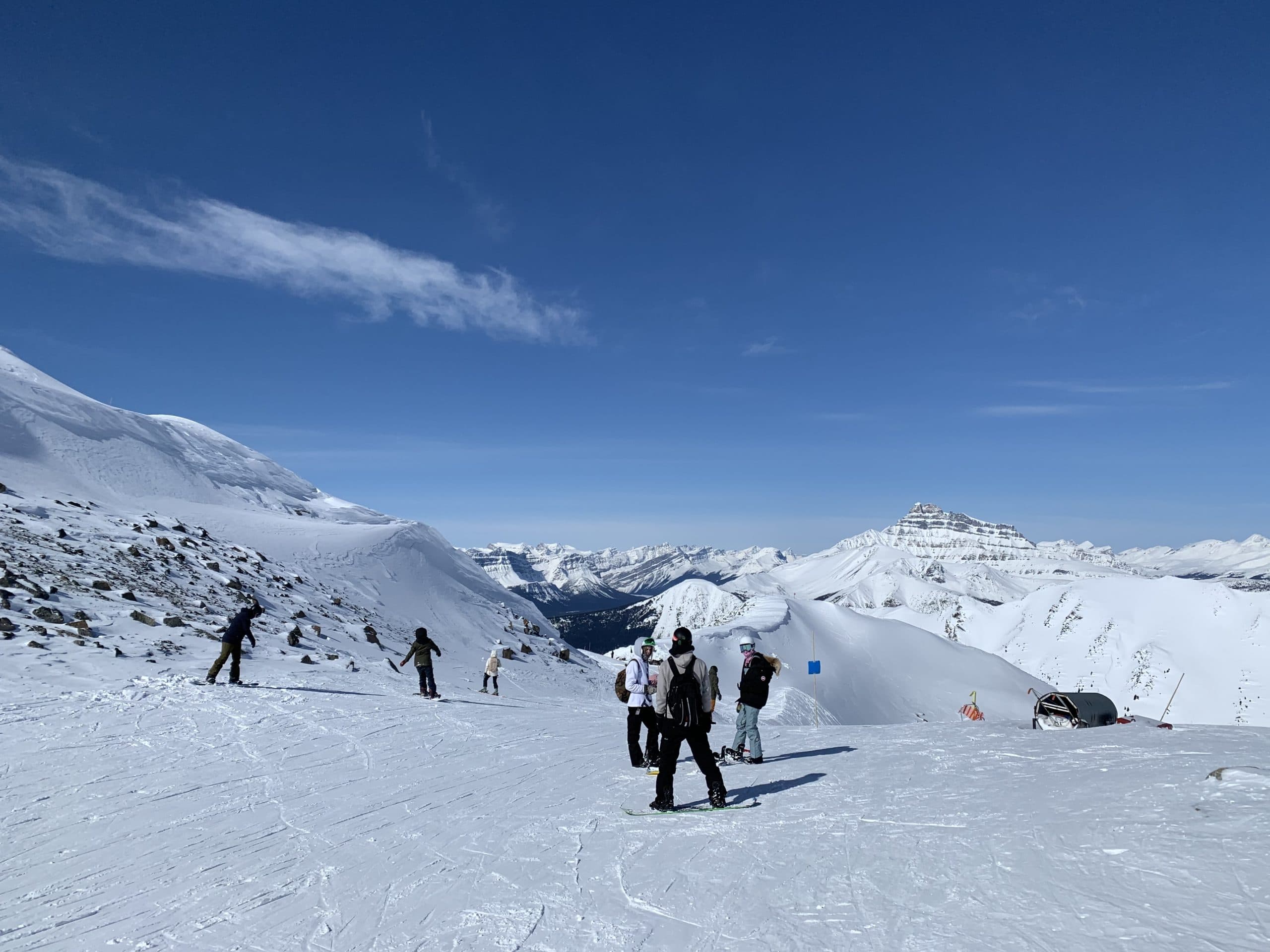 Snowboarders and skiers enjoying a bluebird day on the slopes at Lake Louise Ski Resort, surrounded by breathtaking snow-covered peaks and sweeping views of the Canadian Rockies.