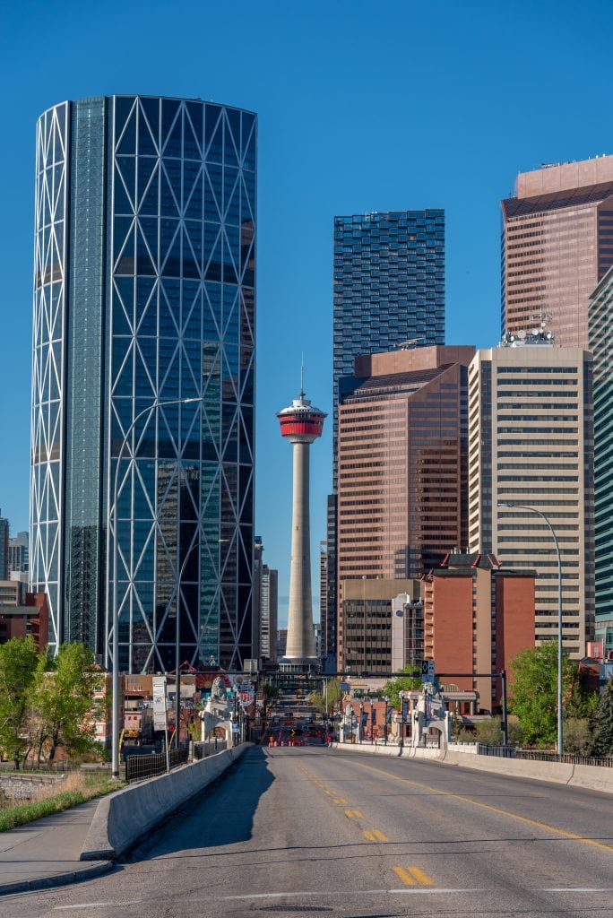 Downtown Calgary skyline framed by modern skyscrapers and the Calgary Tower, viewed from Centre Street Bridge under a clear blue sky on a bright spring morning.