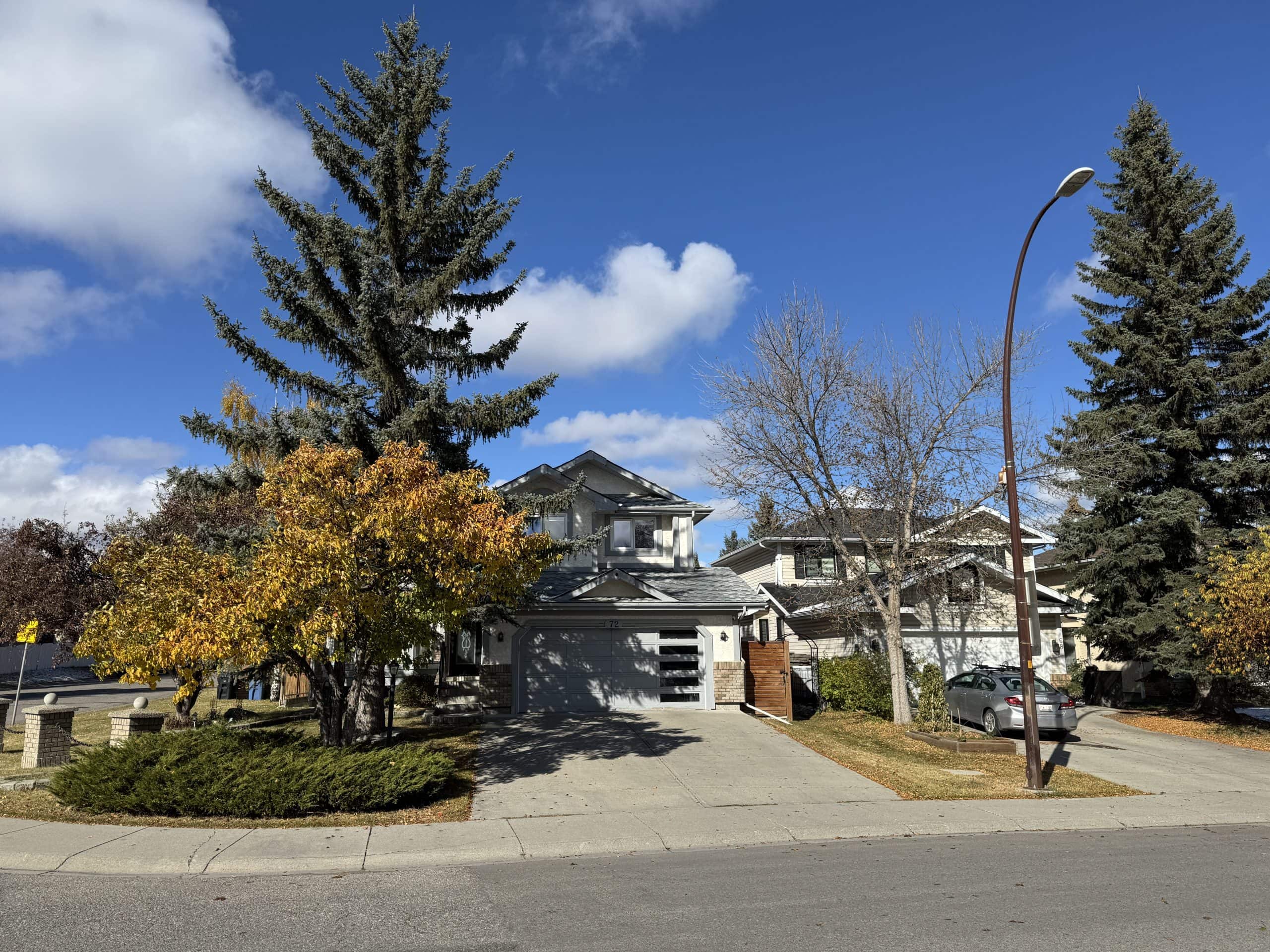 Single family homes on a quiet Shawnessy Calgary street with large mature trees, autumn colours, and a clear blue sky on a sunny fall day.