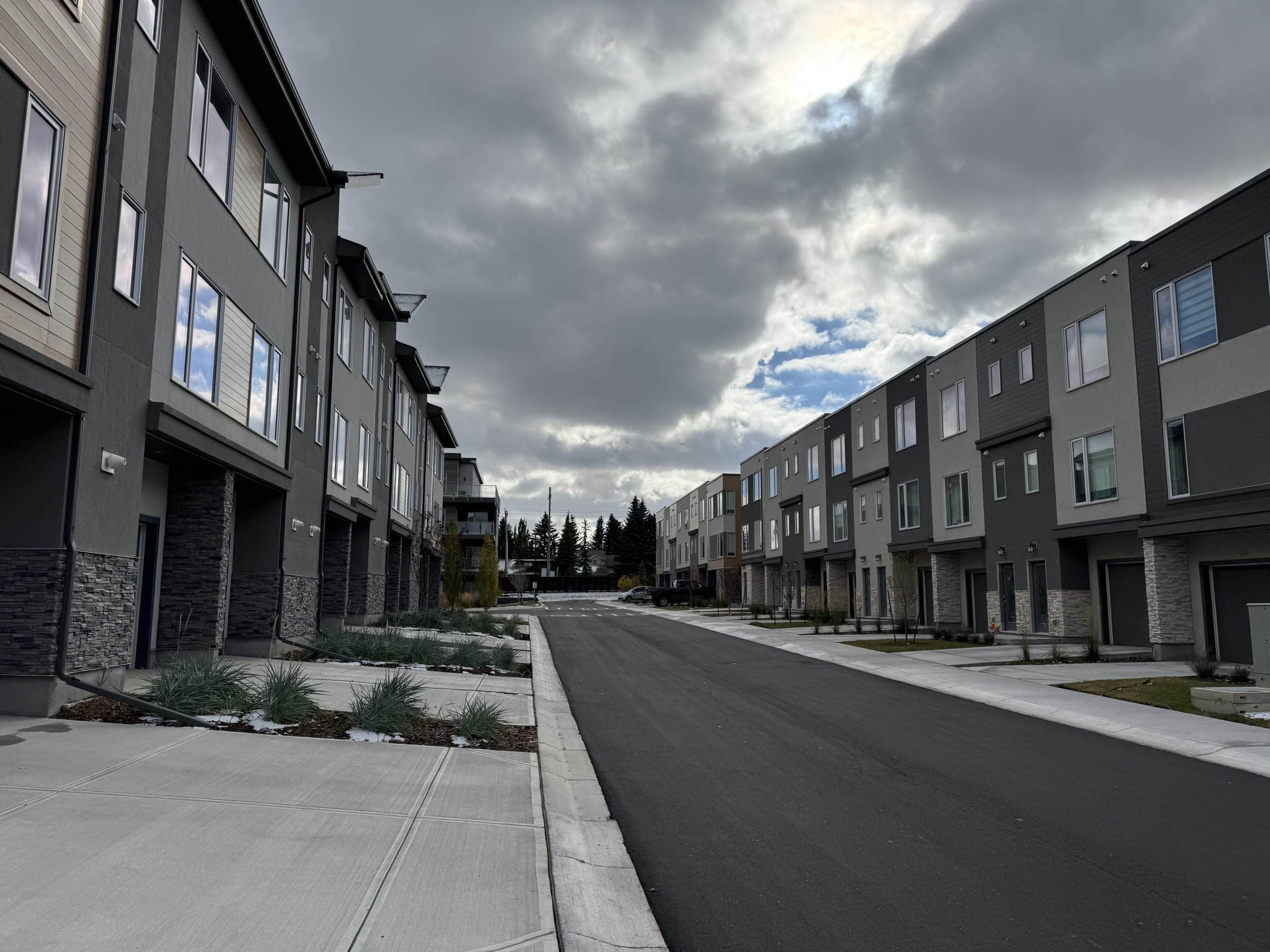 Modern townhomes in Shawnee Slopes Calgary lining a newly paved street under a dramatic cloudy sky, showcasing the neighbourhood’s contemporary redevelopment.