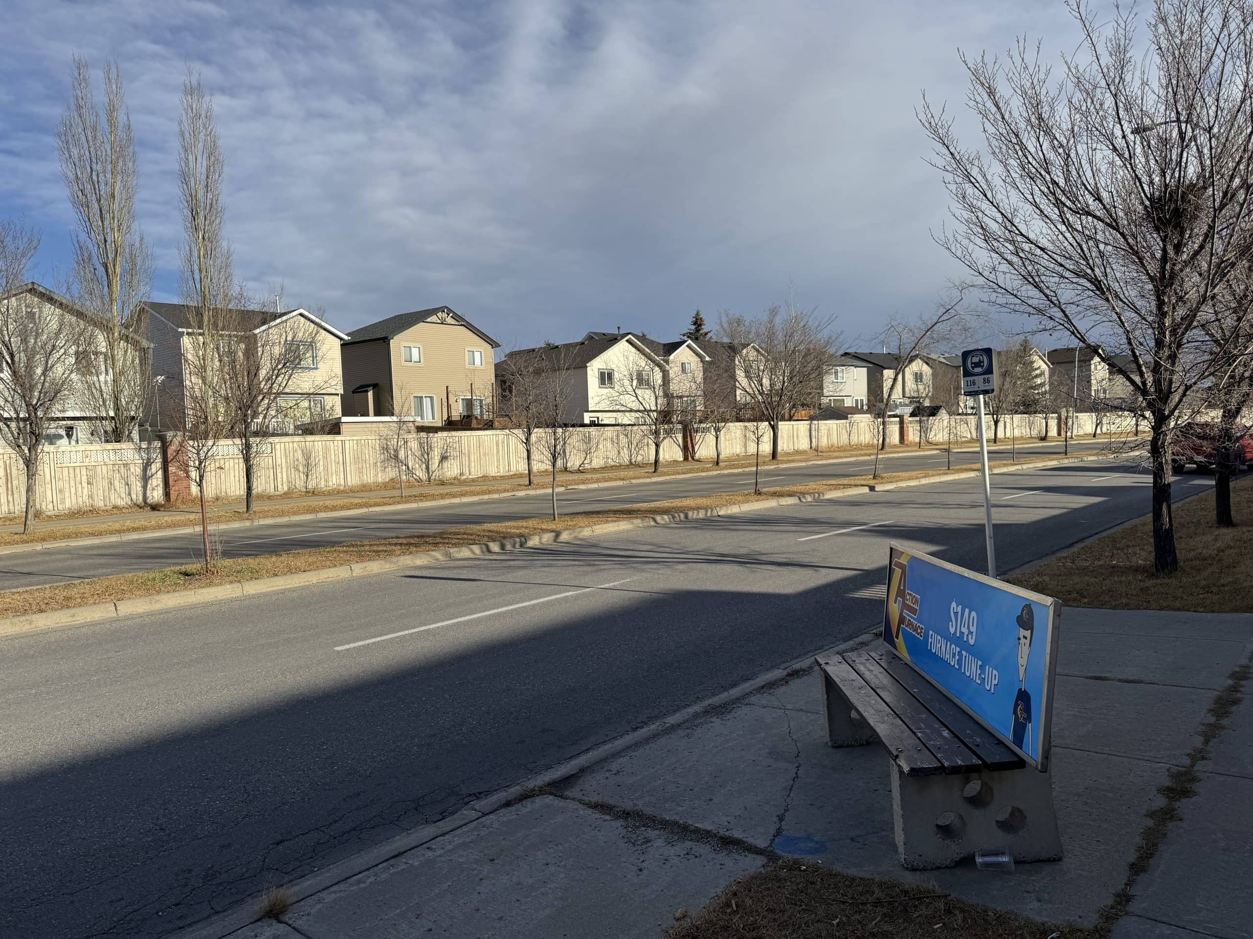 Bus stop along Coventry Hills Way in northeast Calgary with residential homes in the background, showing convenient public transit access for local commuters.