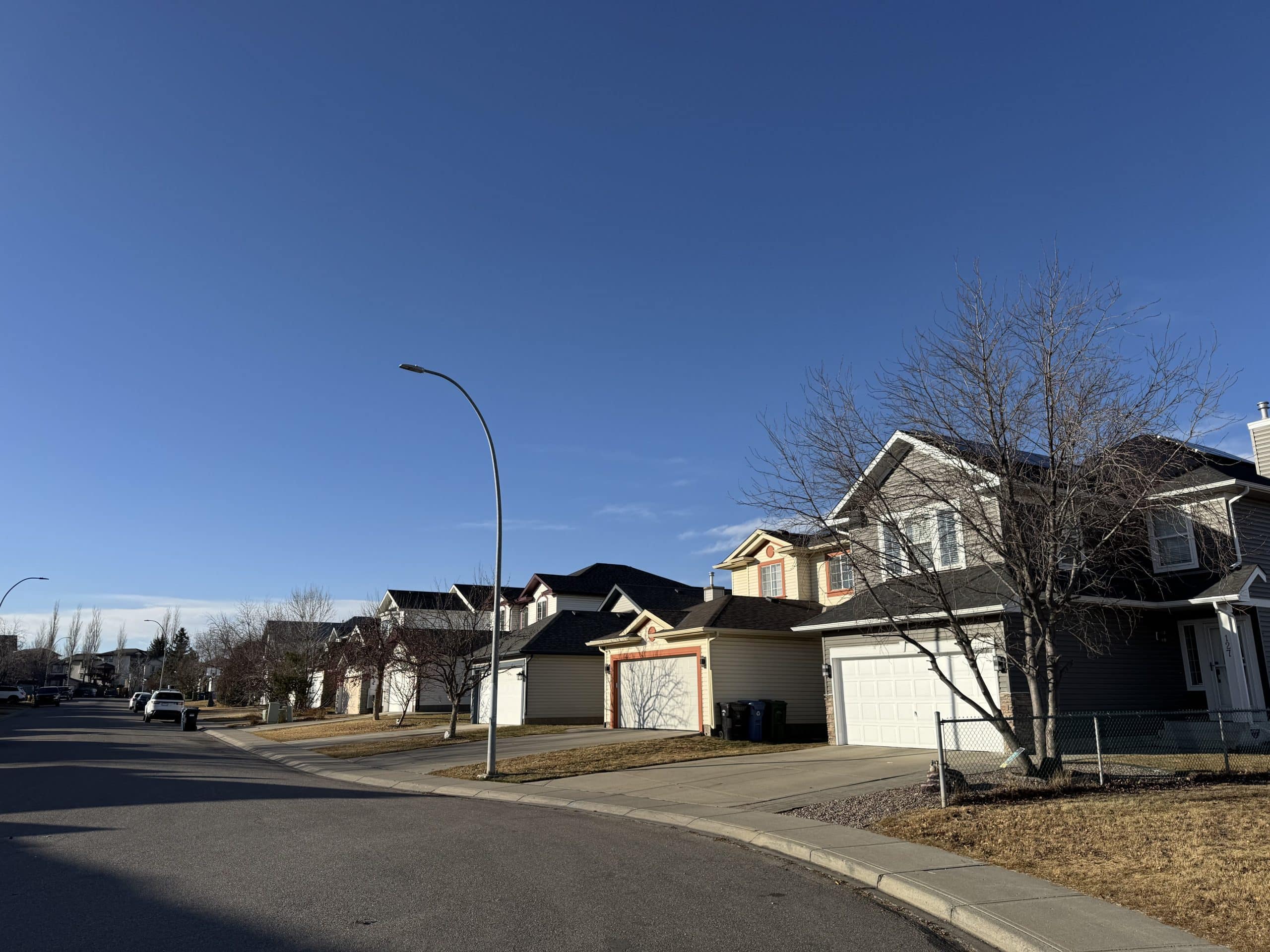 Quiet residential street in Coventry Hills Calgary lined with detached family homes, showcasing the community’s suburban character and affordable real estate options.