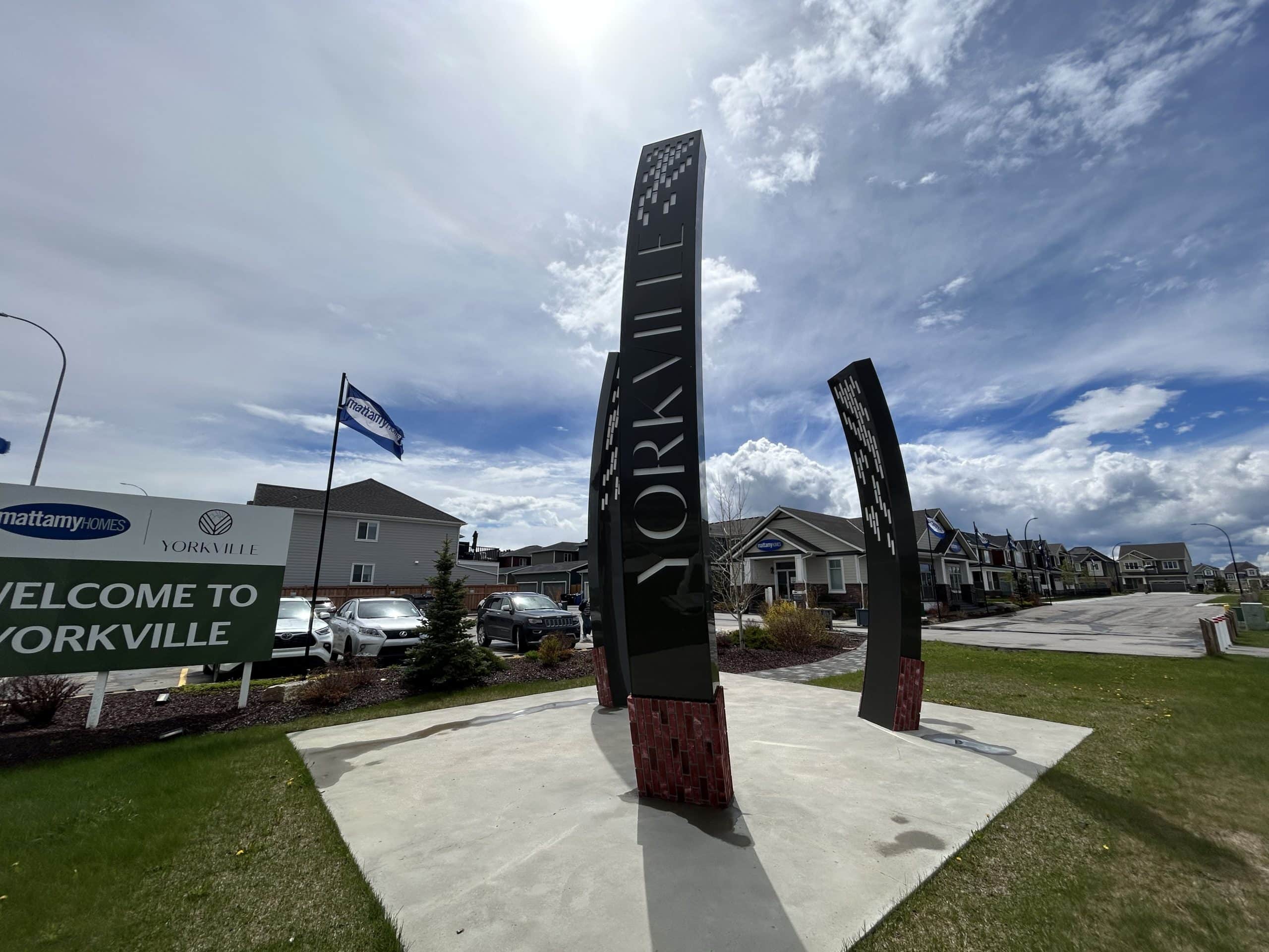 Yorkville Calgary community entrance sign with modern black pillars and residential streets in the background under a bright sky.