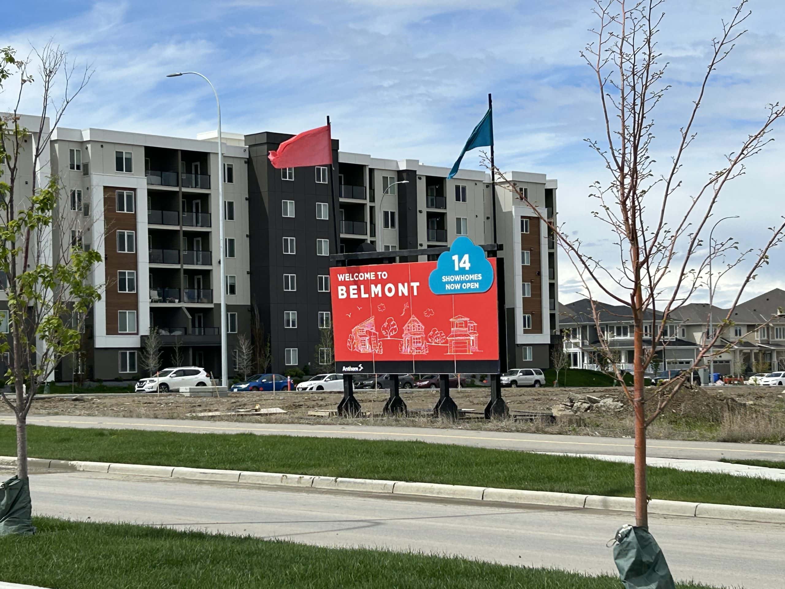 A welcome sign for Belmont, a new community in southwest Calgary, stands in front of modern low-rise condo buildings and nearby single-family homes. The photo highlights new construction and residential growth in one of Calgary’s emerging neighbourhoods.