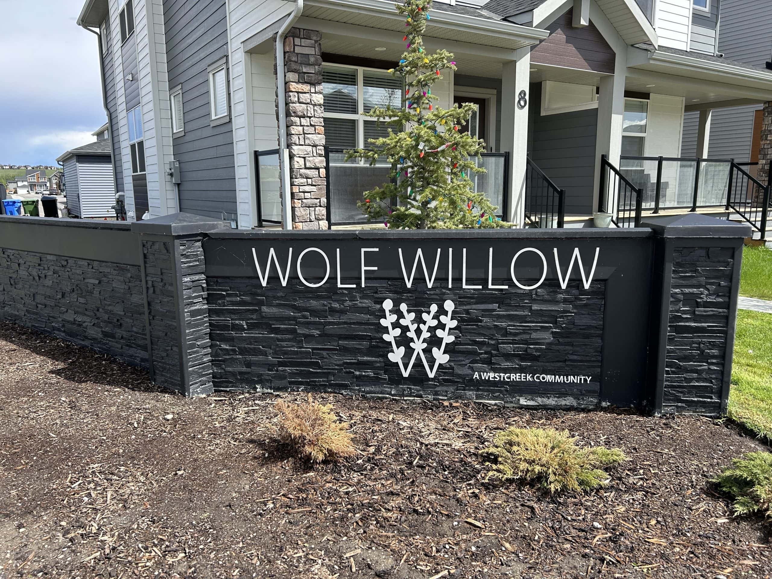 Entry sign for Wolf Willow Calgary featuring a modern black stone design with the community logo in front of newly built homes.