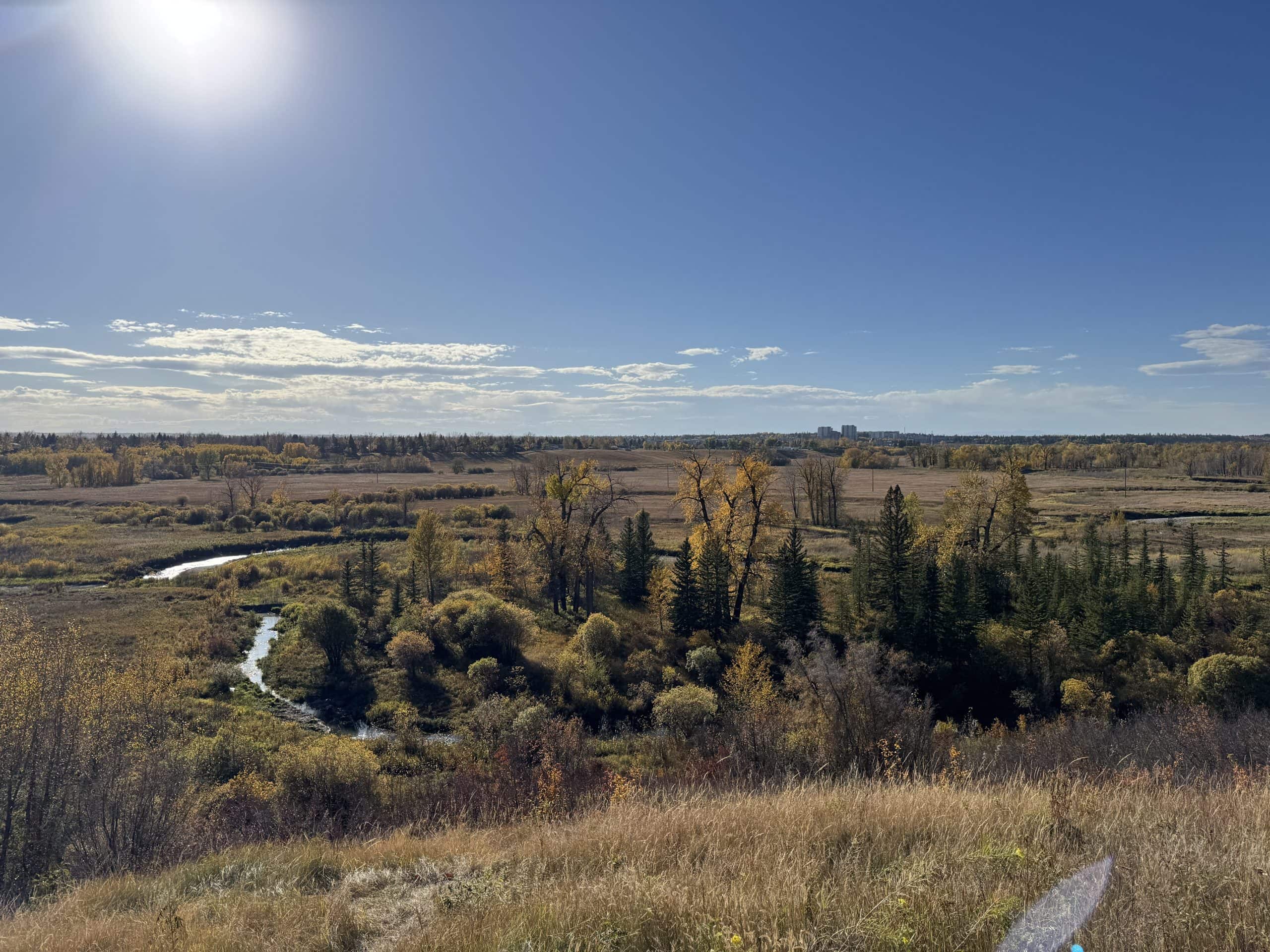 Wide ridge view in Parkland overlooking Fish Creek Park with fall trees, open fields, and a bright sunny sky.