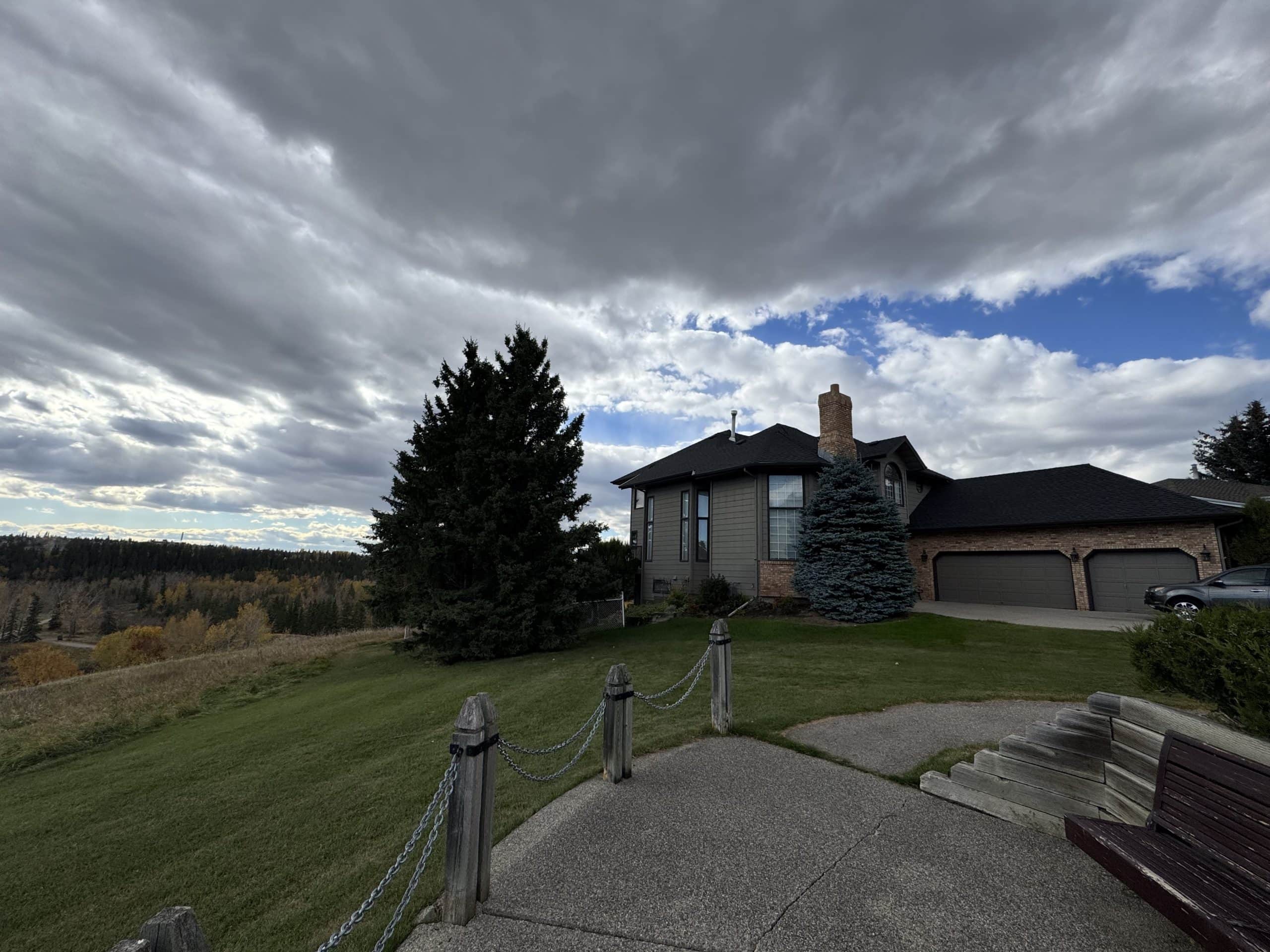 Large home in Canyon Meadows overlooking green space and wooded areas with dramatic clouds and patches of blue sky.