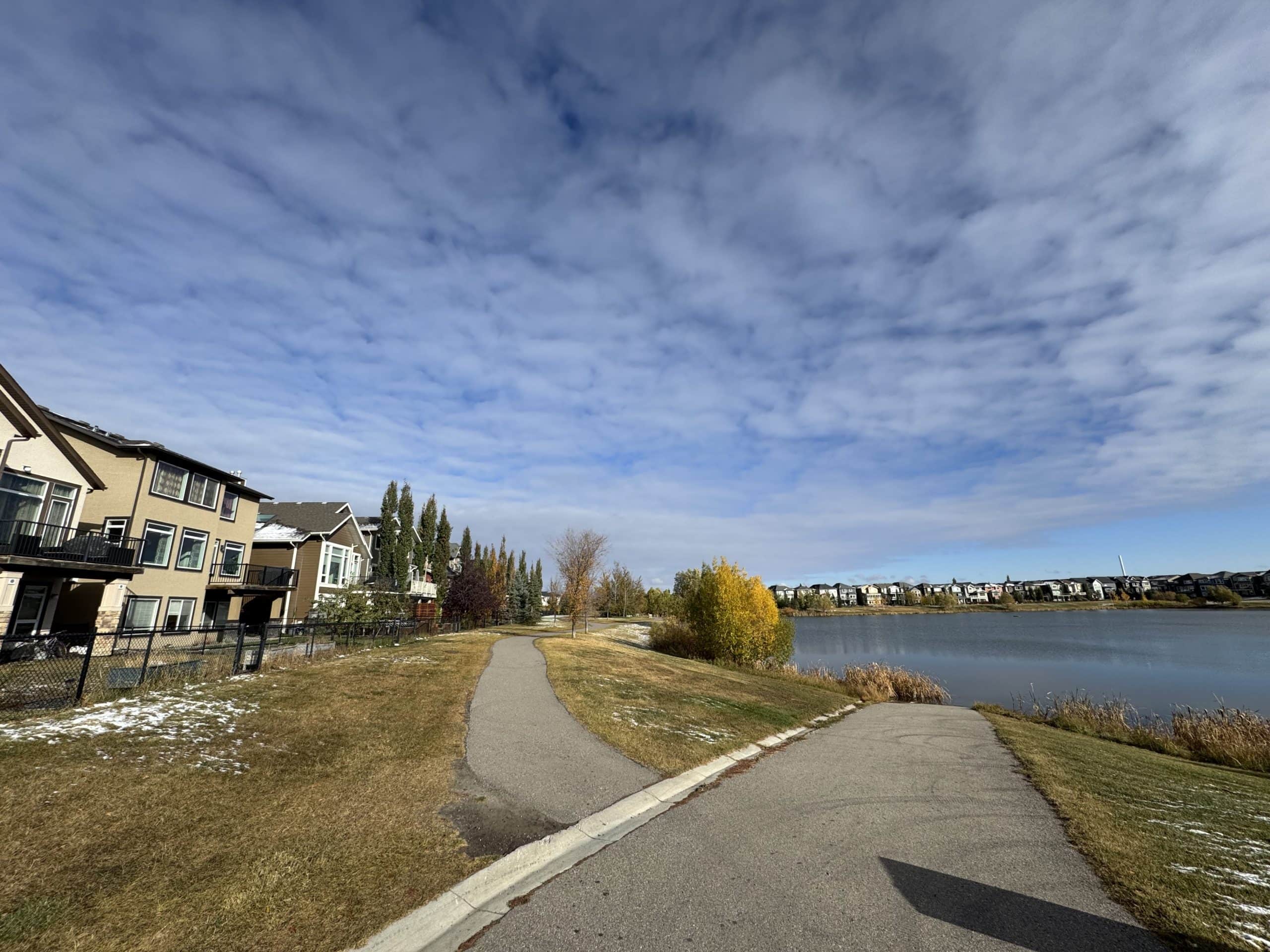 Peaceful walking paths along the Legacy community pond in south Calgary, with lakeside homes, fall colours, and wide open skies.