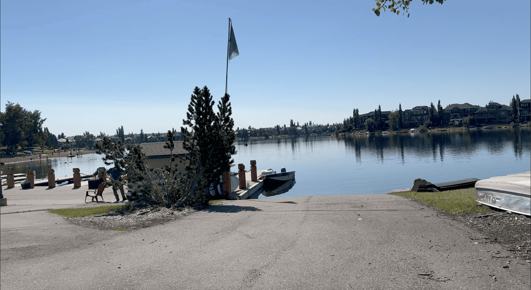Lake Chaparral in Calgary on a sunny summer day with calm water, docks, a small boat, and lakeside homes in the background.
