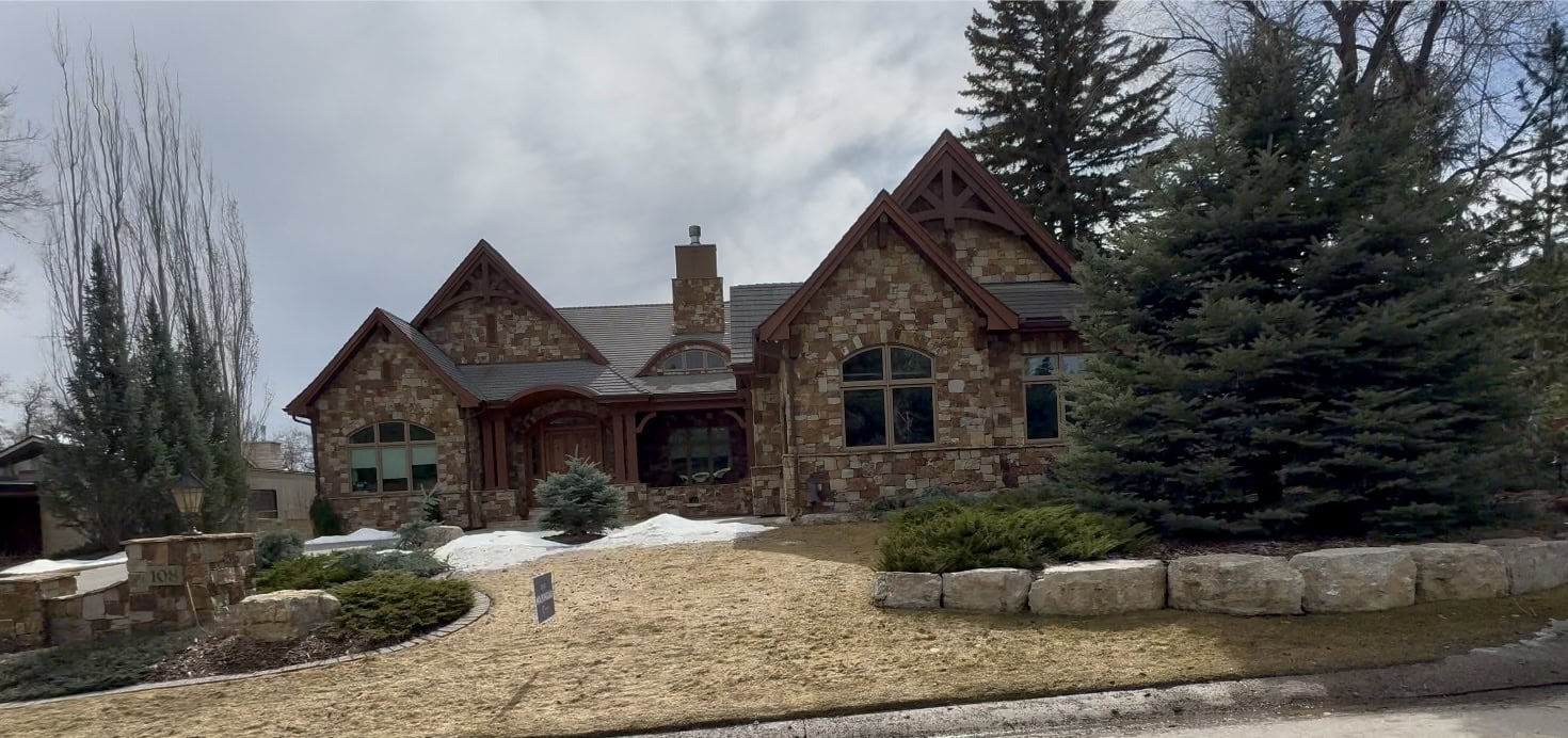 Luxury estate home in Eagle Ridge with stone exterior, grand rooflines, mature evergreens, and a private landscaped front yard on a quiet upscale street in South Calgary.