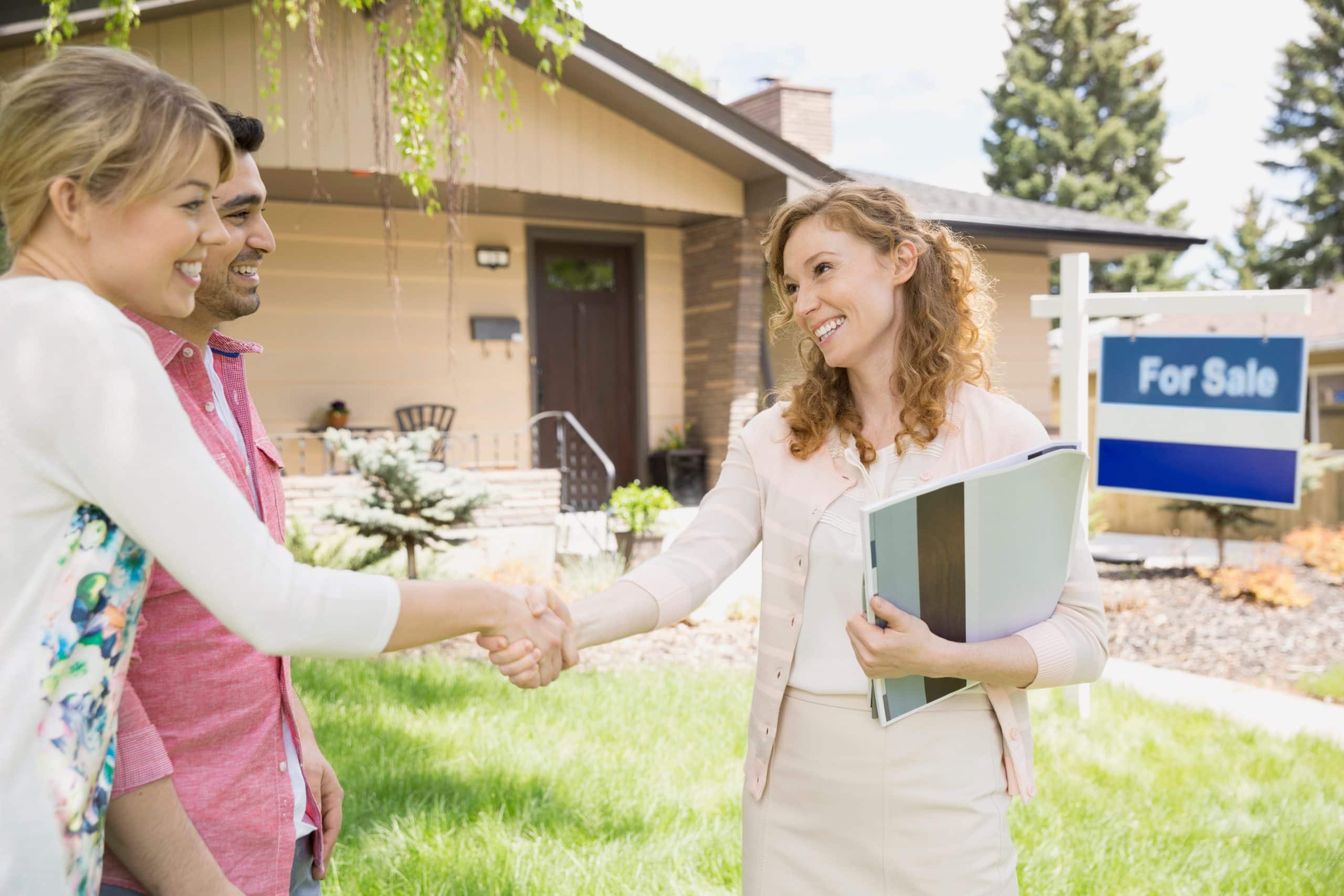 Realtor shaking hands with sellers outside a home for sale, representing professional guidance in the Calgary real estate market.