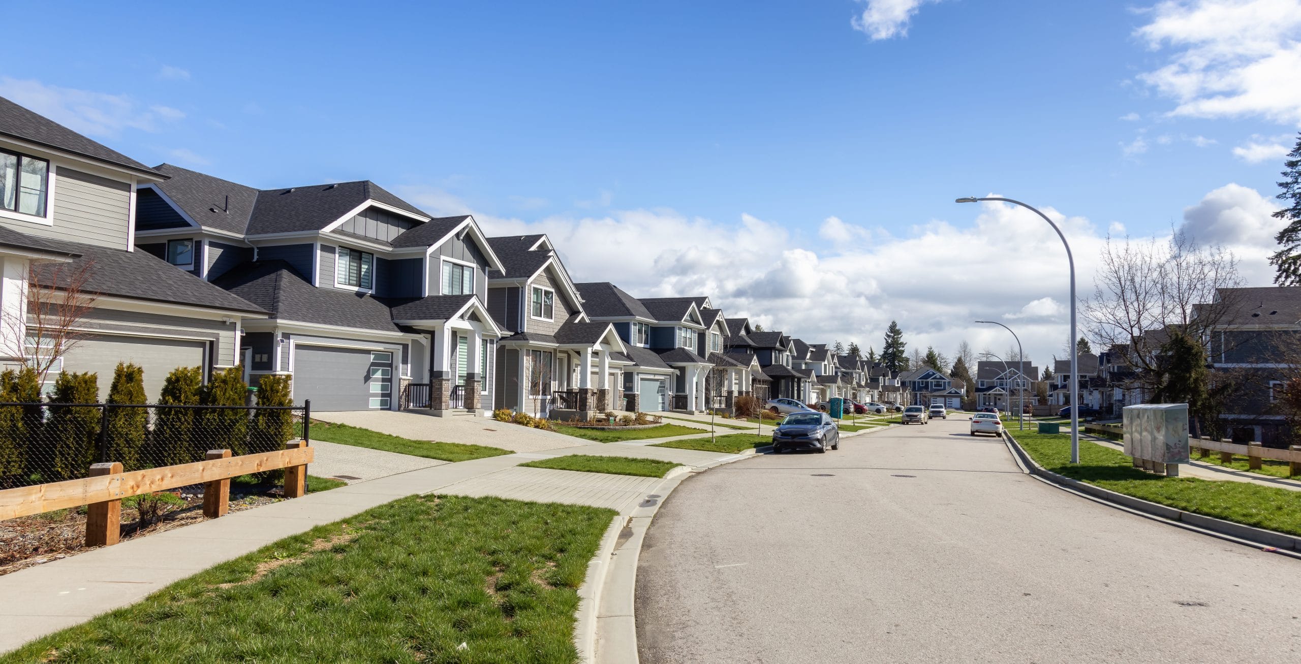 Residential street with modern detached homes in a suburban Calgary neighbourhood on a clear day.
