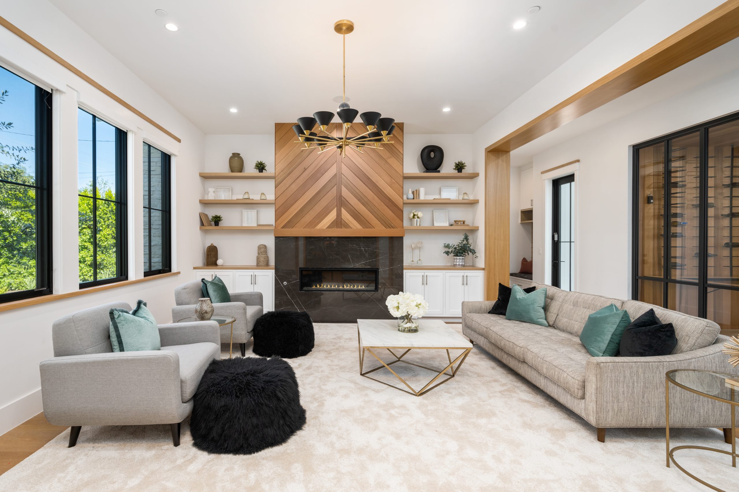 Bright, modern living room with custom fireplace feature wall, built in shelving, and large windows in a luxury home interior.