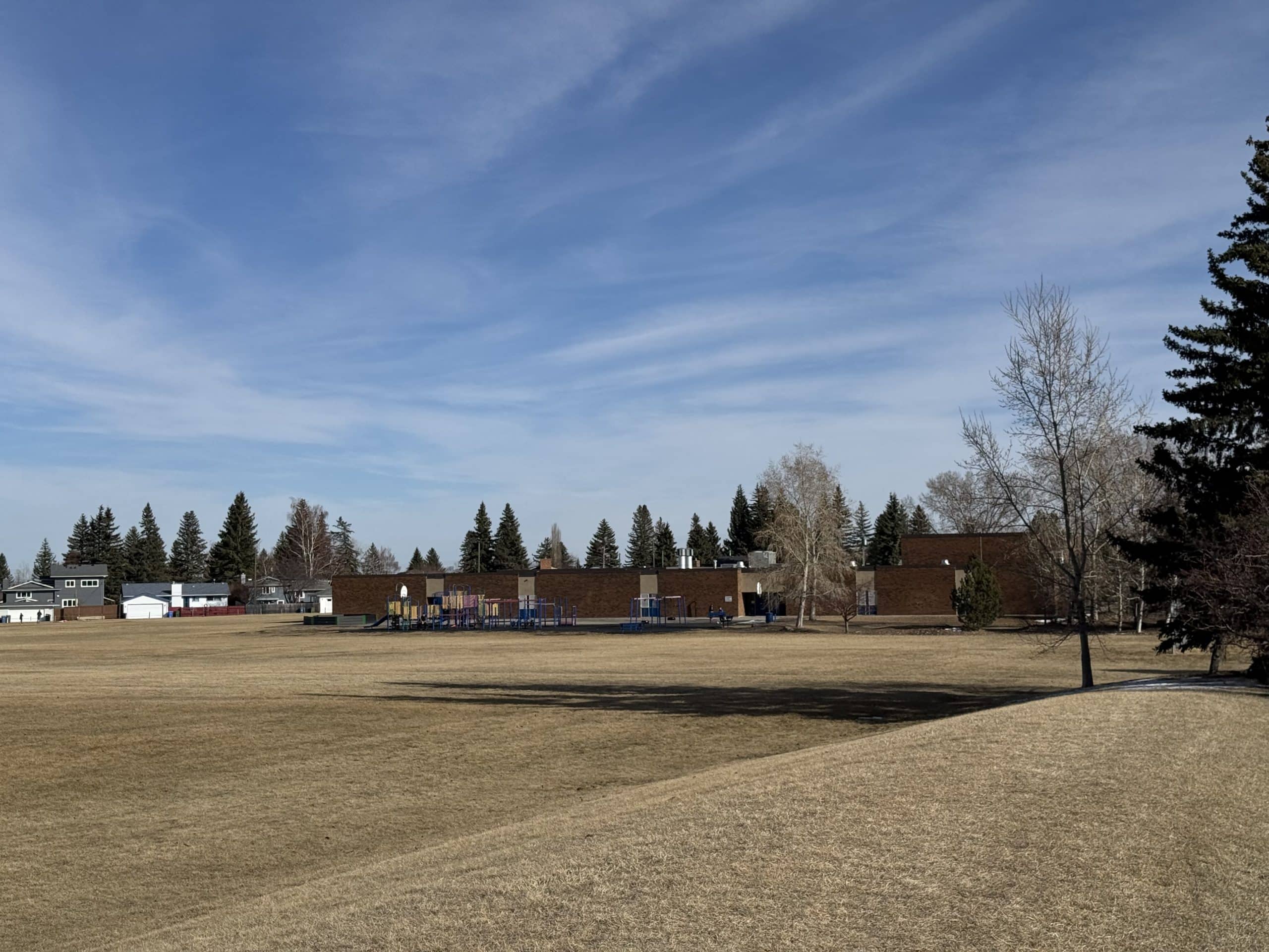 Lake Bonavista Calgary school grounds with open green space, playground, and nearby homes in a family friendly neighbourhood setting