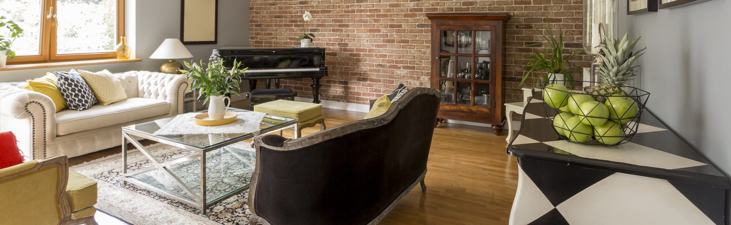 Bright and well staged living room with hardwood floors, brick accent wall, piano, and stylish furniture showcasing a warm and inviting interior design.