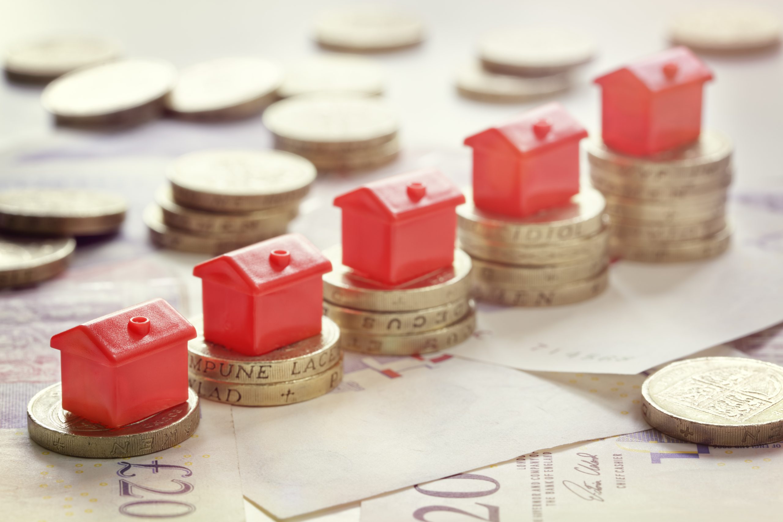 Red house models stacked on rising piles of coins representing the property ladder, home values, real estate investment, and increasing housing prices.