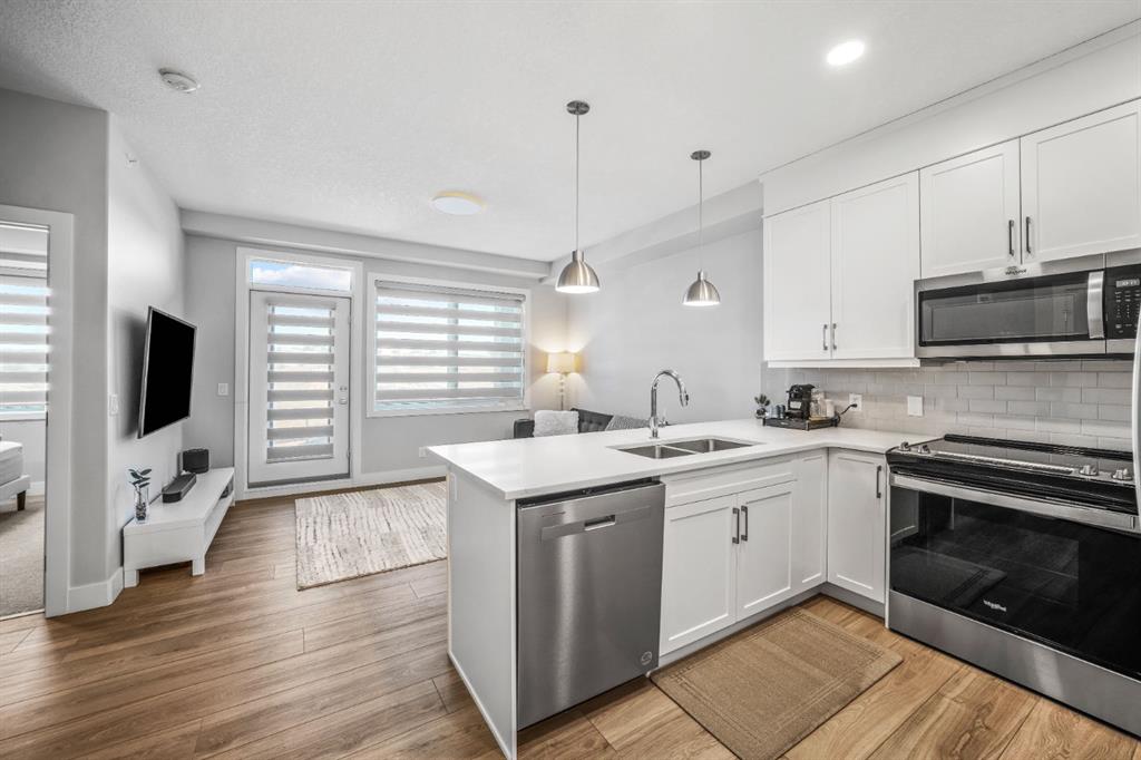 Modern open concept kitchen and living area at 8355 19 Avenue SW #403 in Springbank Hill Calgary, featuring quartz countertops, stainless steel appliances, large windows, and bright contemporary finishes