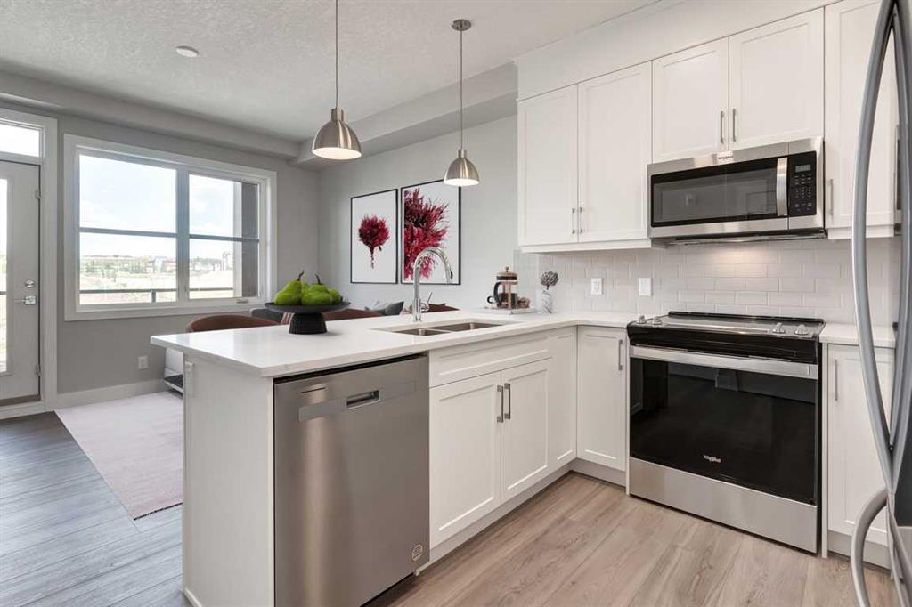 Bright modern kitchen at 8355 19 Avenue SW #403 in Springbank Hill Calgary featuring quartz countertops, stainless steel appliances, white cabinetry, and an open concept layout with large window for natural light