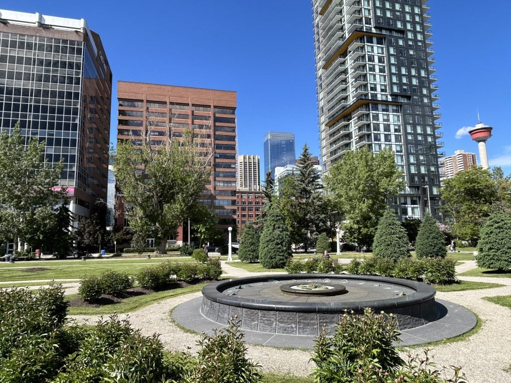 Downtown Calgary park surrounded by modern condo towers and skyline views near the Beltline and Calgary Tower on a sunny summer day.