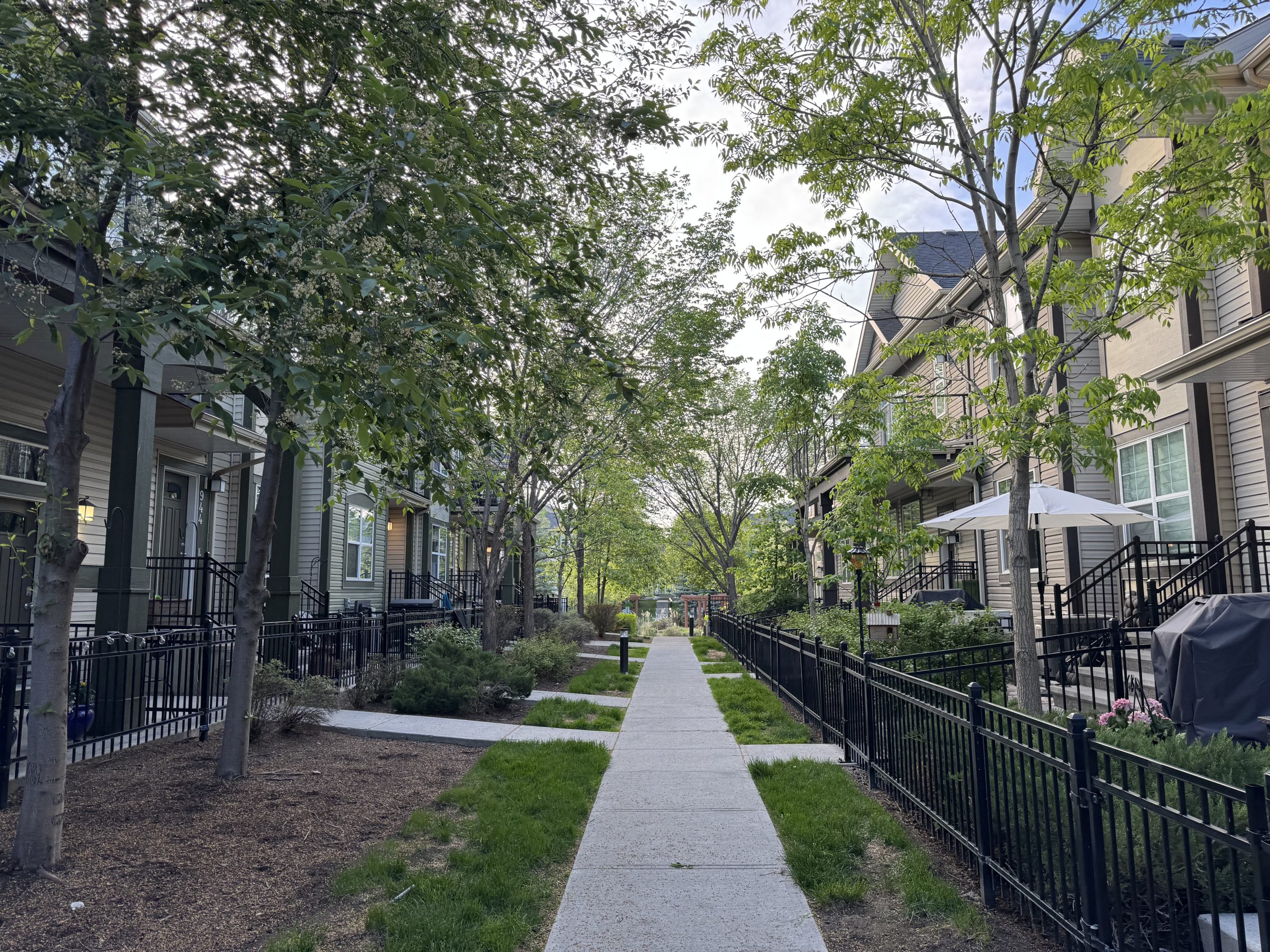 Tree lined pedestrian pathway between homes in McKenzie Towne, showcasing the community's walkable design, landscaped green spaces, front porch lifestyle, and neighbourhood connectivity that help create its unique small town atmosphere within Calgary.