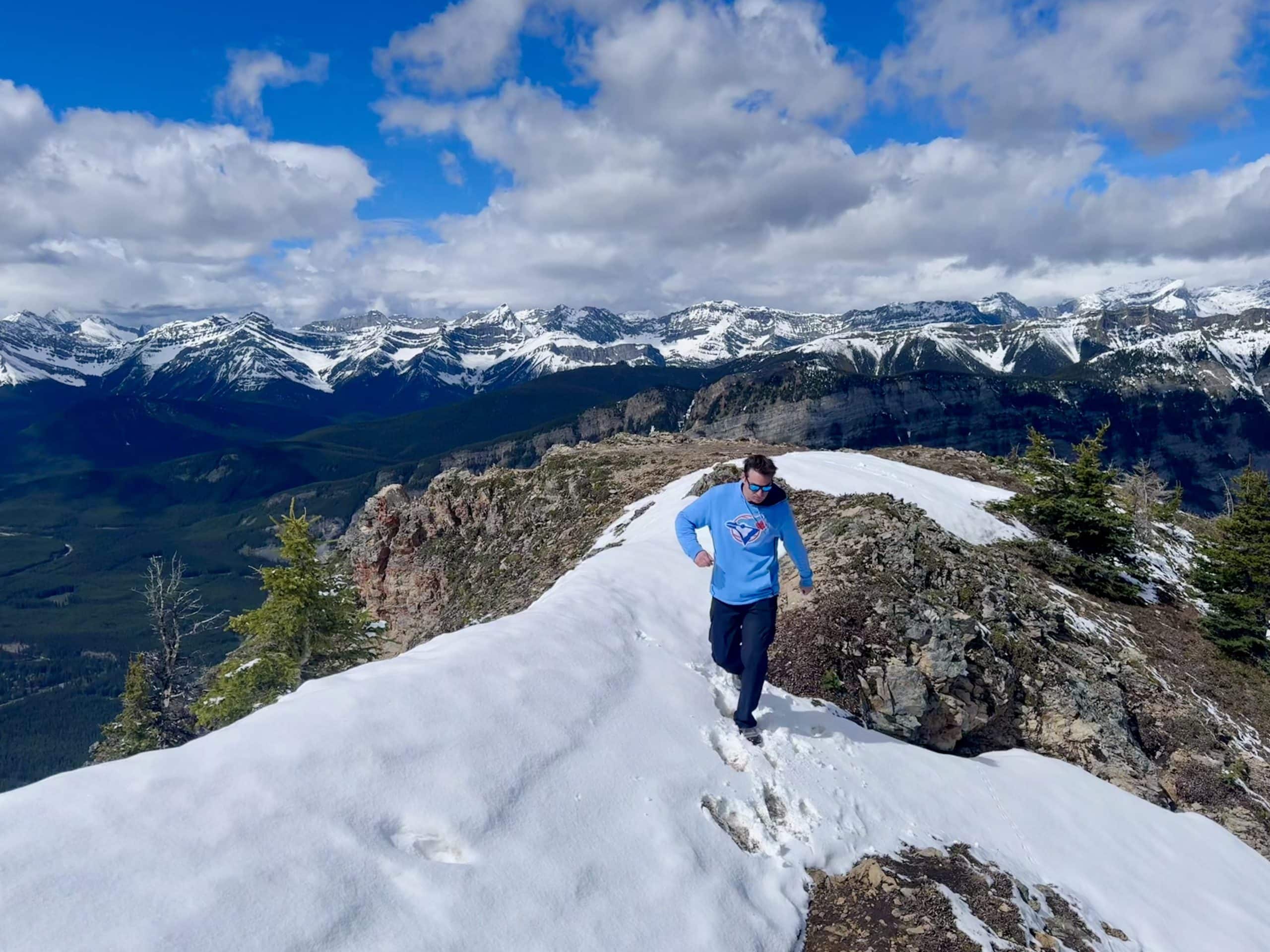 Hiker crossing a lingering snow patch near the summit ridge of King Creek Ridge in Kananaskis Country during mid June.