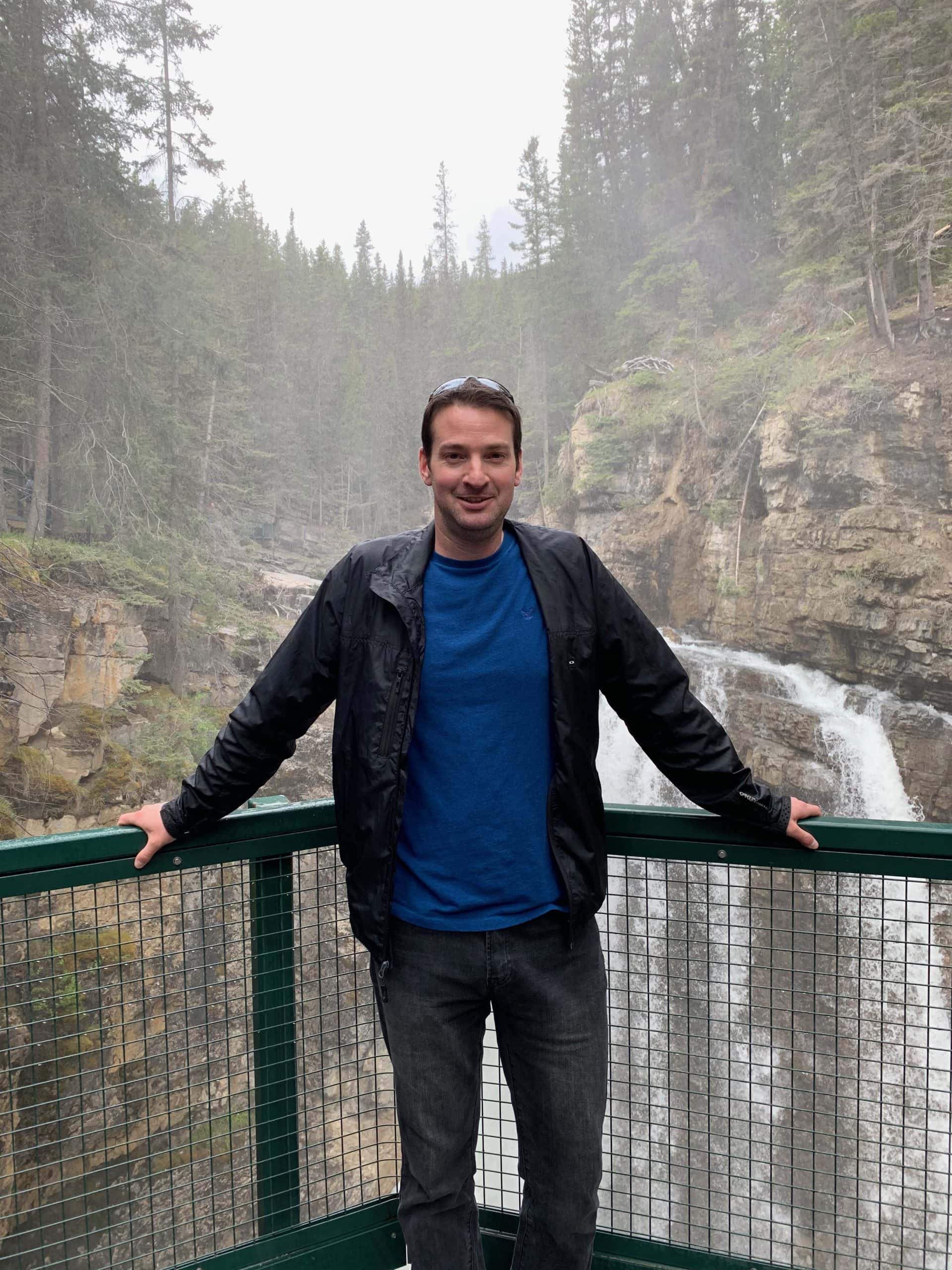 Ryan Gillard at Johnston Canyon in Banff National Park, with a waterfall and forested canyon in the background.
