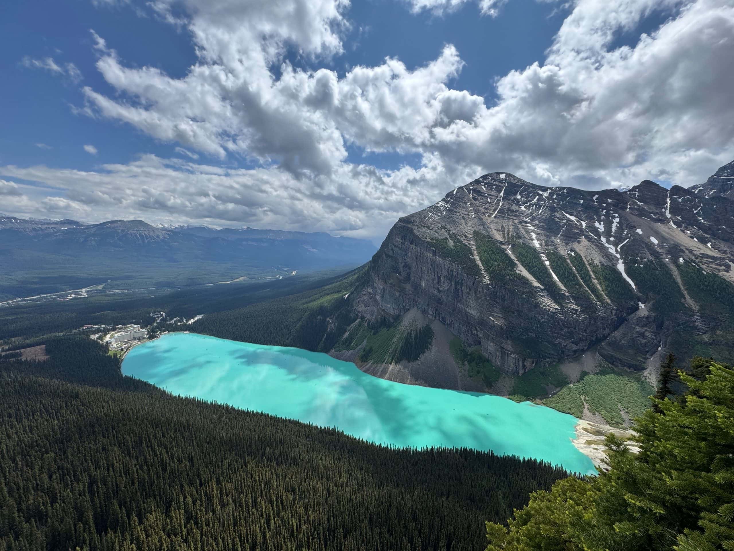 Turquoise waters of Lake Louise surrounded by forest and snow-capped Rocky Mountains in Banff National Park, Alberta.