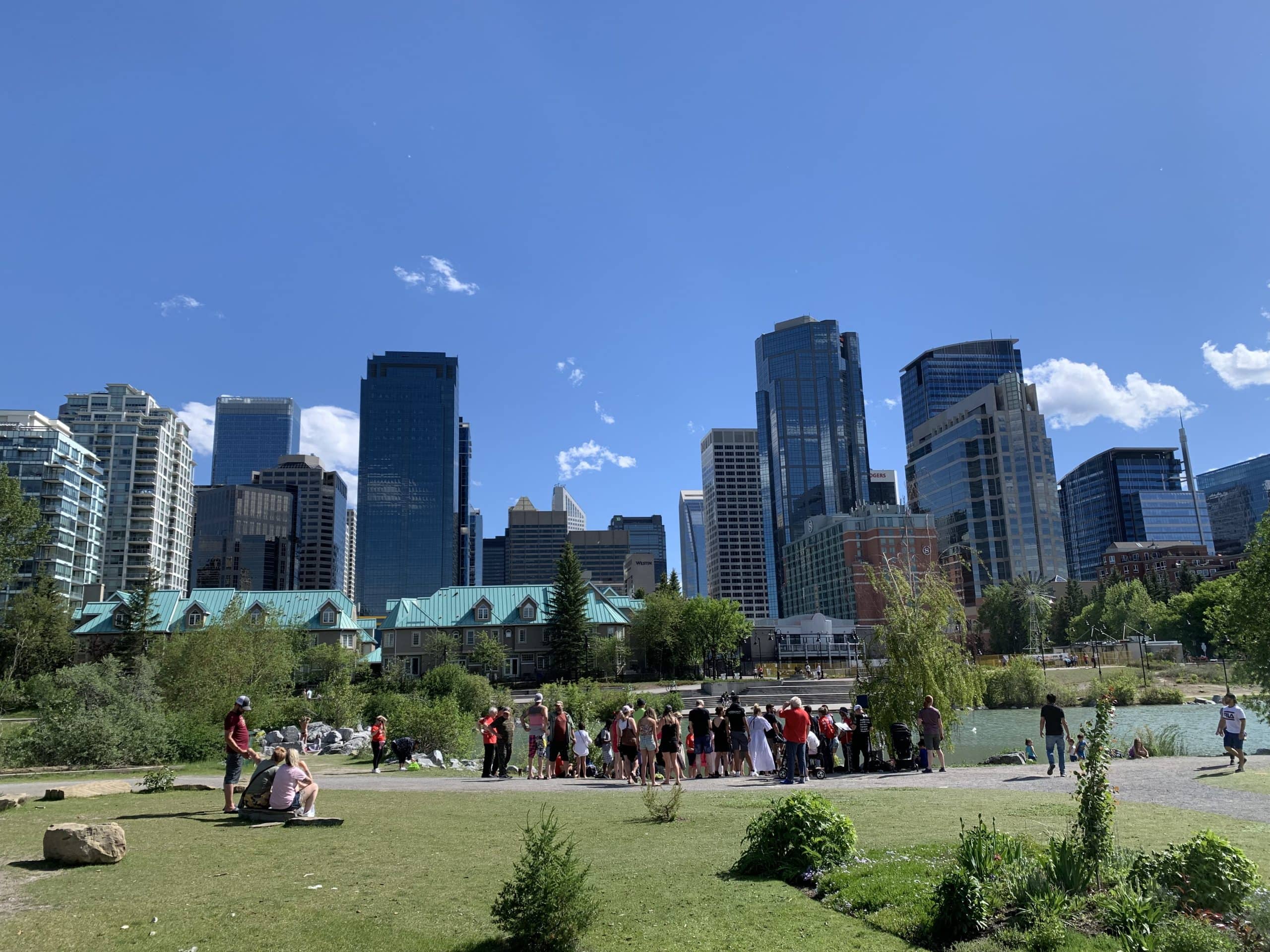 Prince’s Island Park with people enjoying the Bow River pathways and downtown Calgary skyline on a sunny summer day.