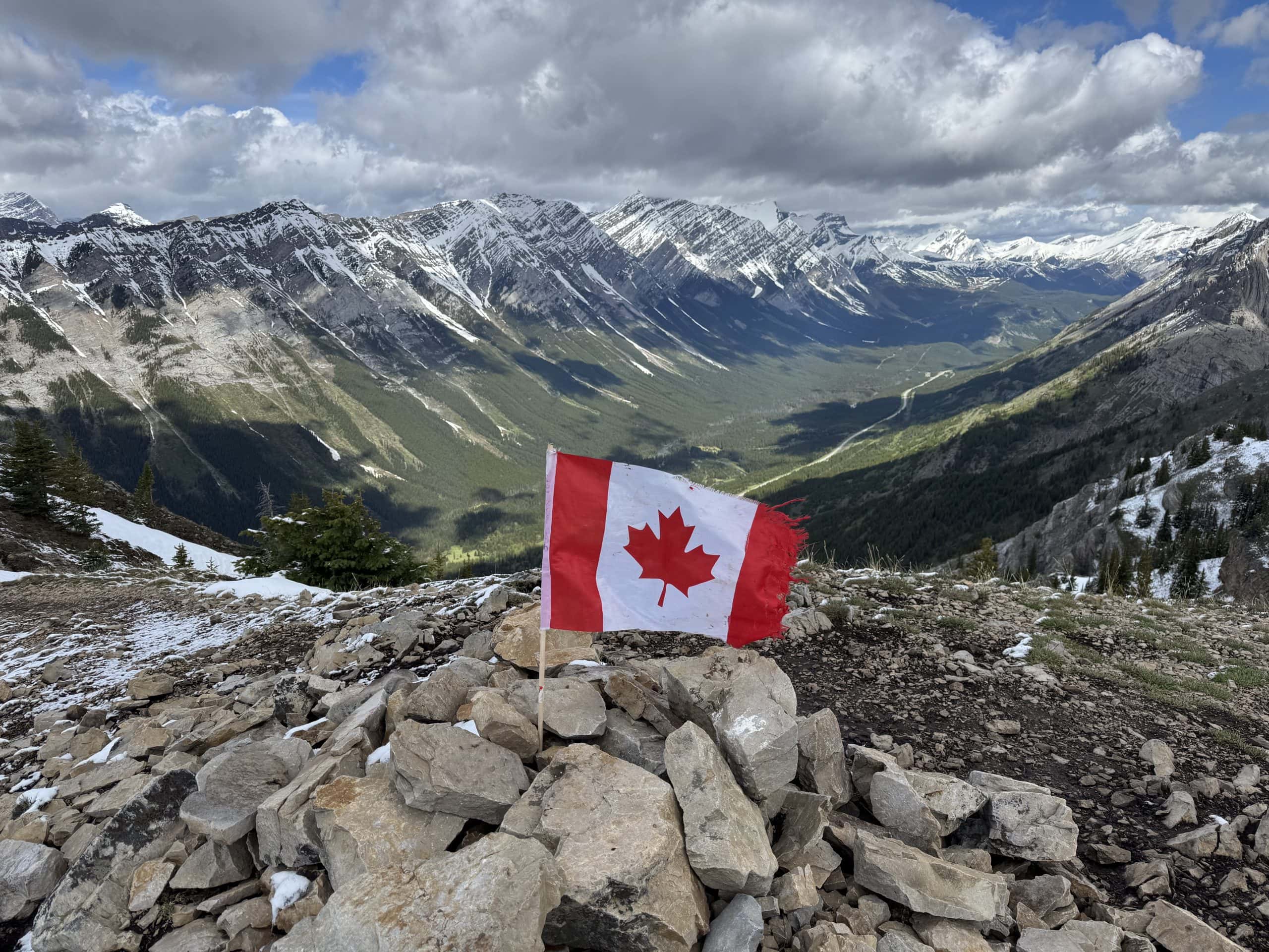 Canadian flag overlooking a snow capped Rocky Mountain valley in Kananaskis, Alberta.