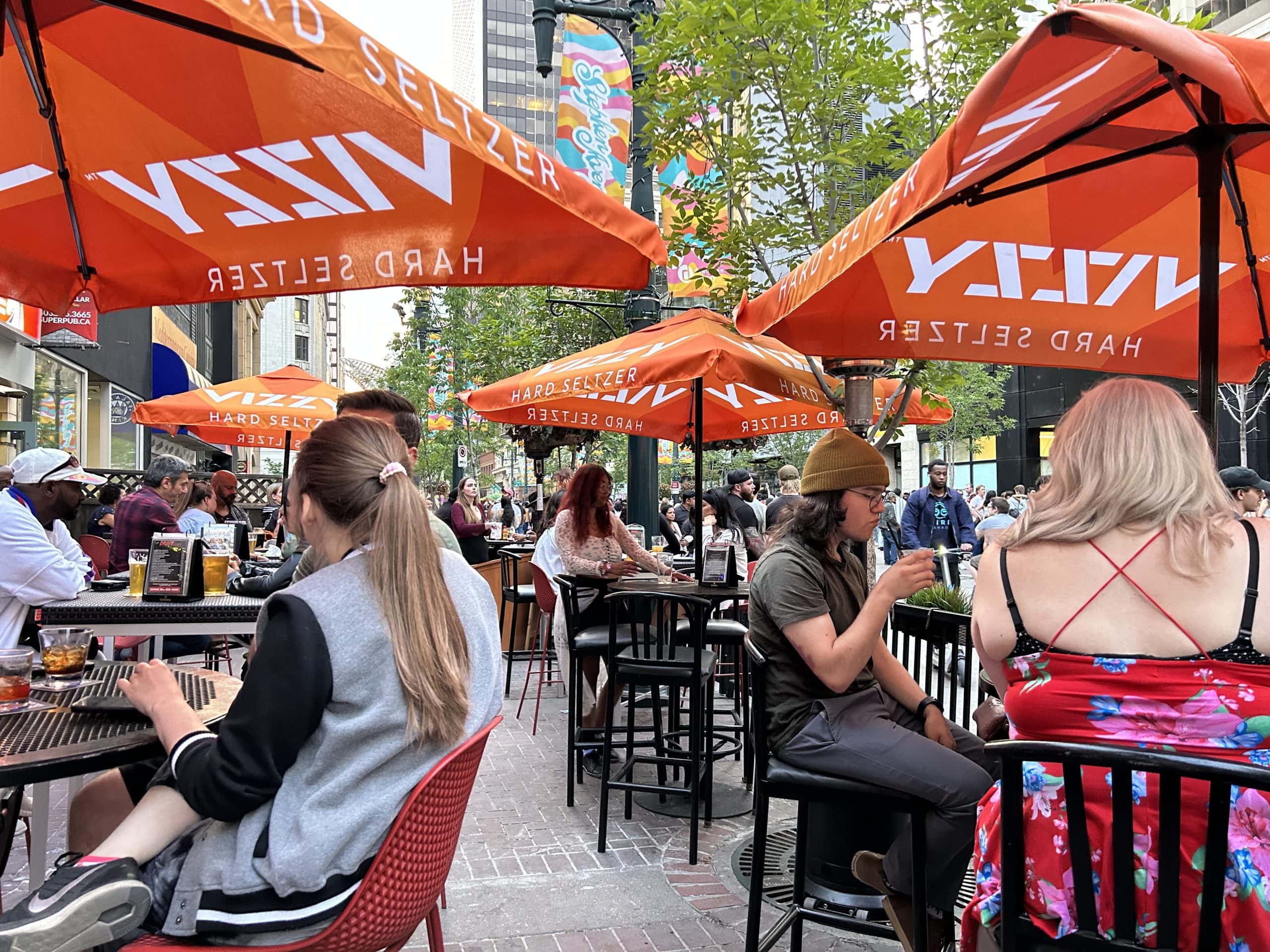 Lively outdoor patio in downtown Calgary with people enjoying food and drinks on a sunny summer day.