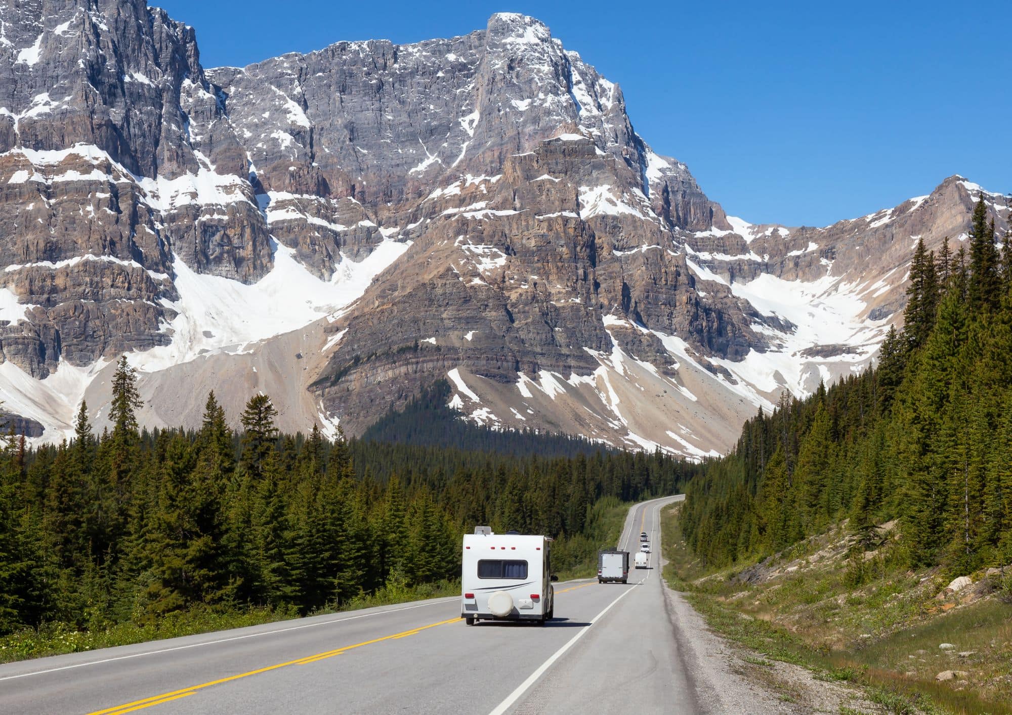 Mountain highway through the Canadian Rockies with vehicles travelling beneath snow-capped peaks in Alberta.