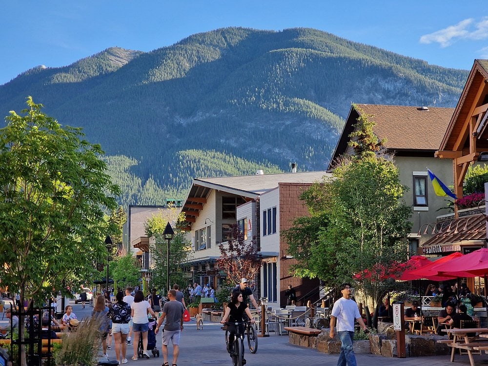 Banff Avenue in downtown Banff, Alberta, with shops, restaurants, patios and Rocky Mountain scenery surrounding the town.