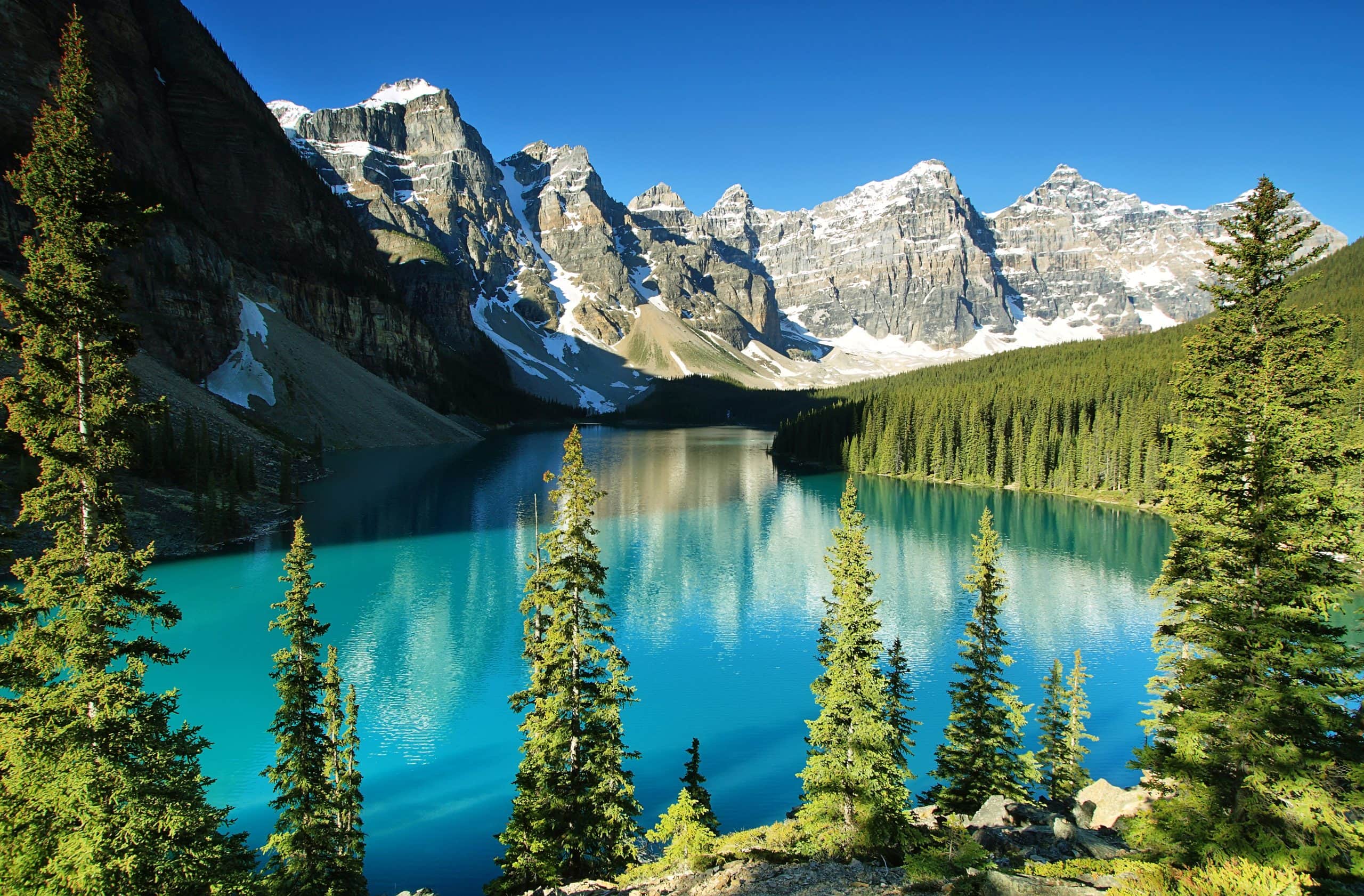 Turquoise waters of Moraine Lake surrounded by evergreen forest and the Canadian Rockies in Banff National Park, Alberta.